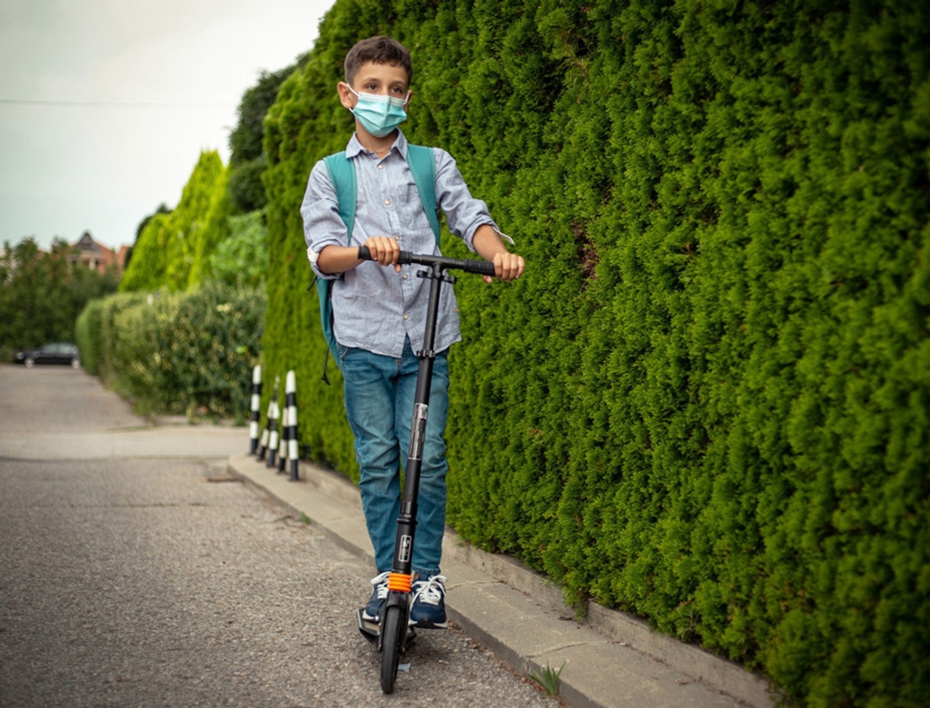 Boy with a protective face mask pushing his scooter to shool. Serbia