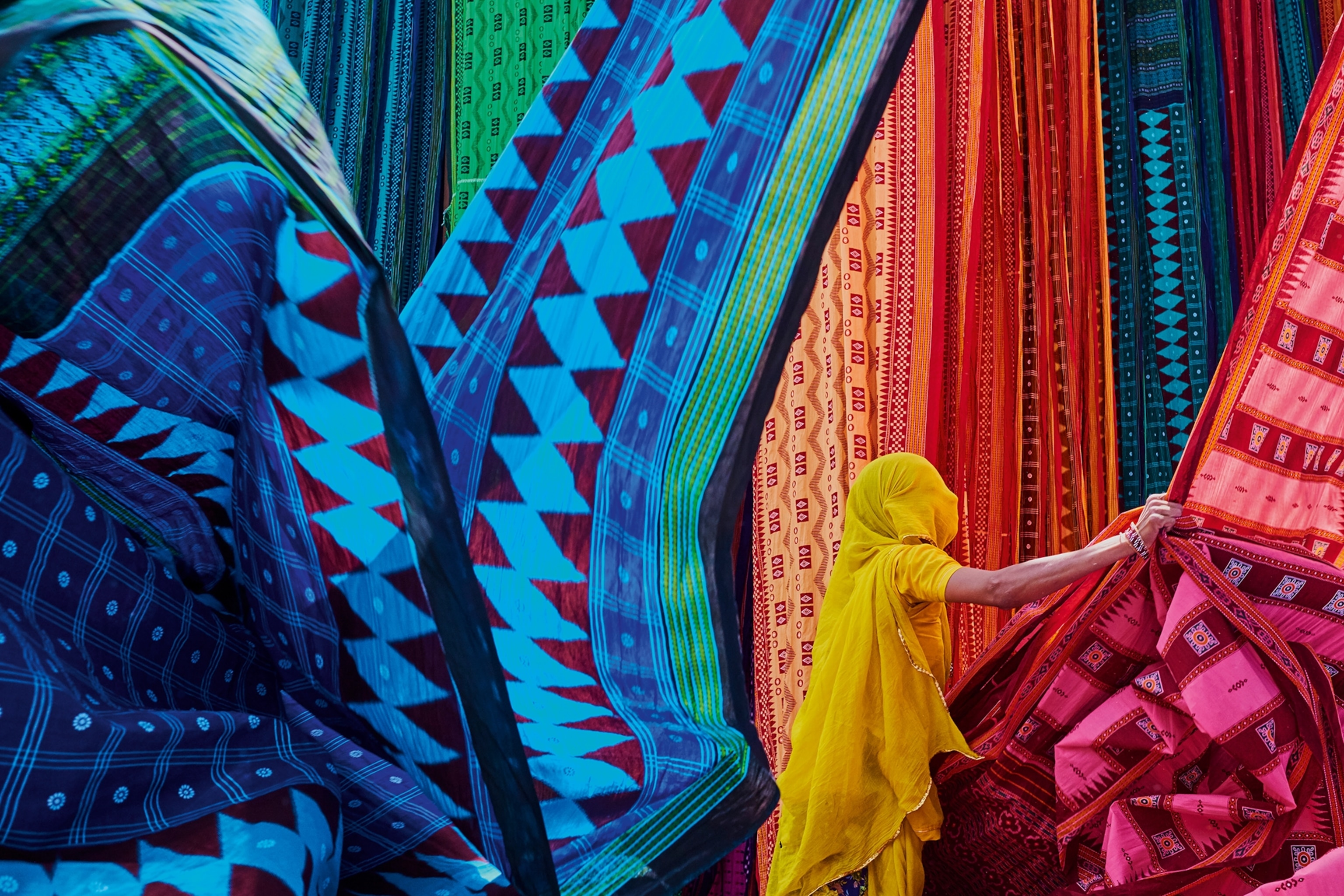 A female, veiled figure in the midst of long, flowing sari fabrics.