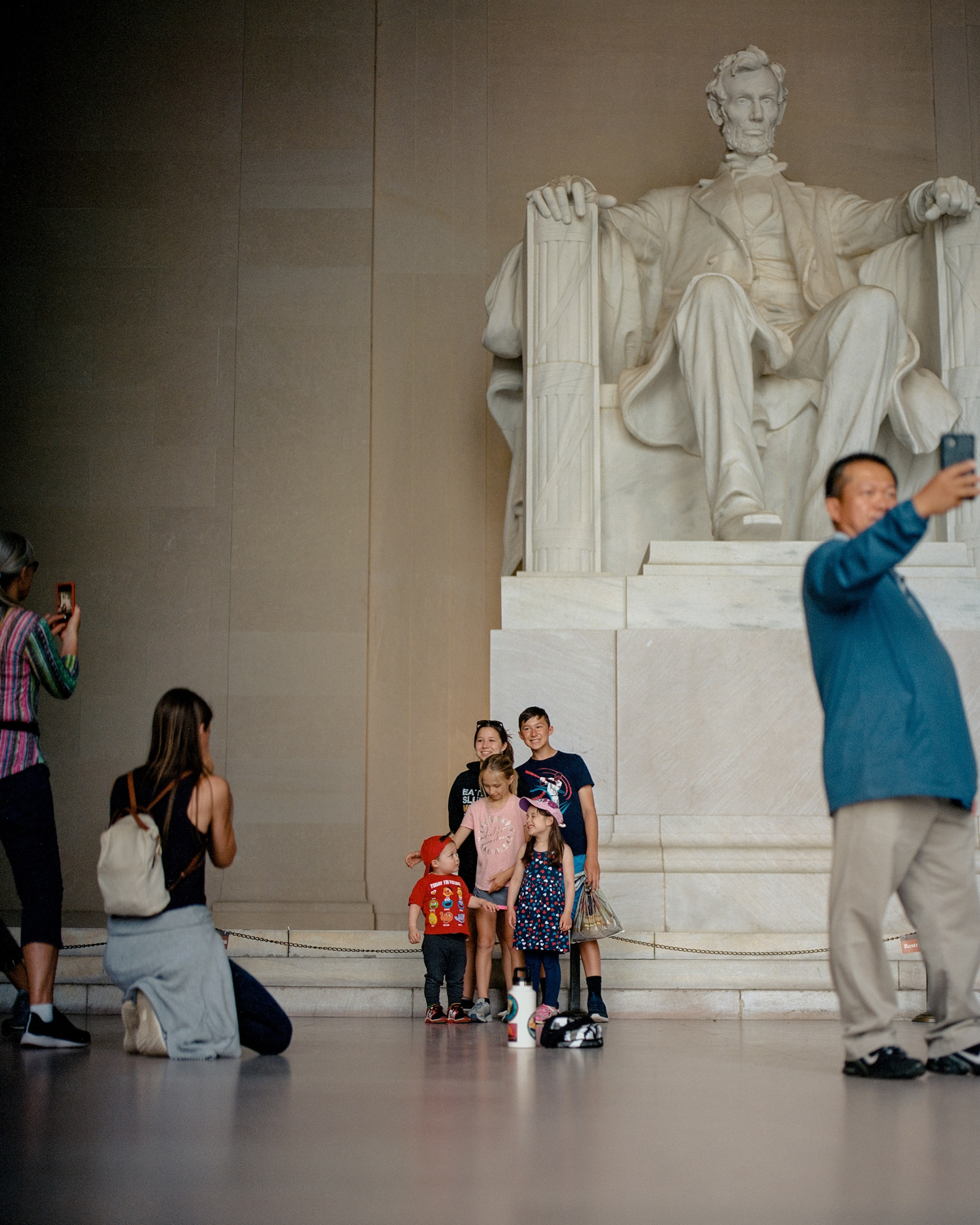 A family stands for a phone portrait amid other people taking their own photos inside the chamber of the Lincoln Memorial