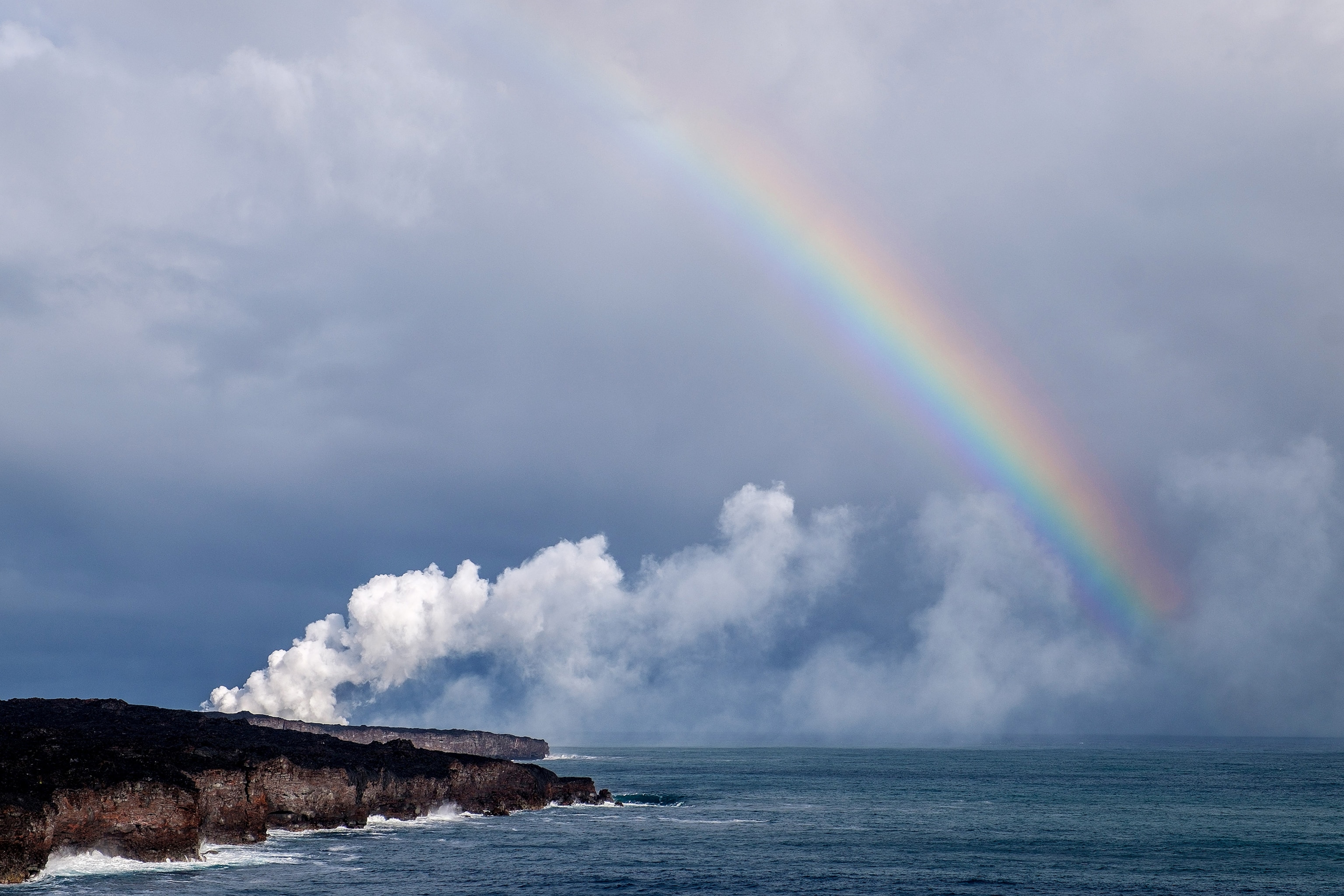 a rainbow arcing over steam from the lava of Kilauea in Hawaii