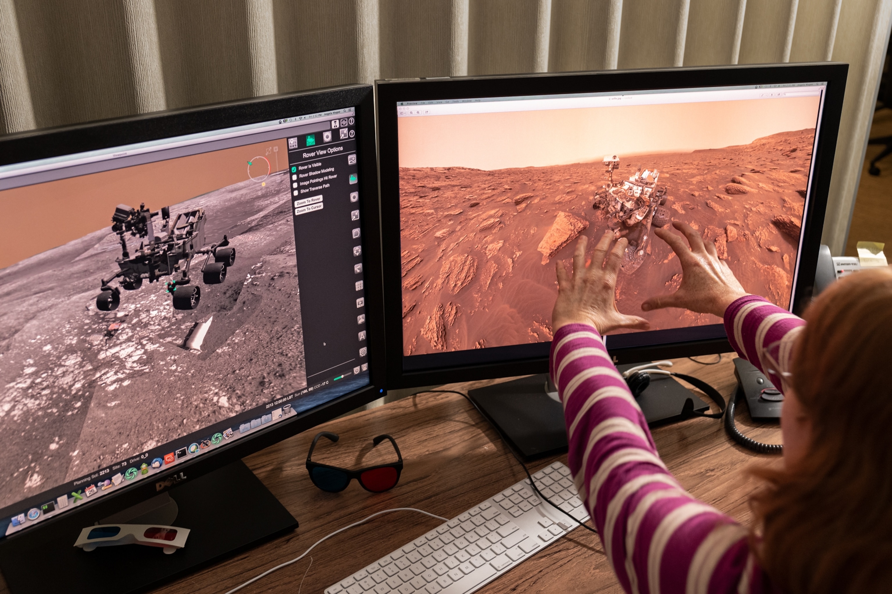 woman stretching her hands to one of two computer monitors with the rover on them.