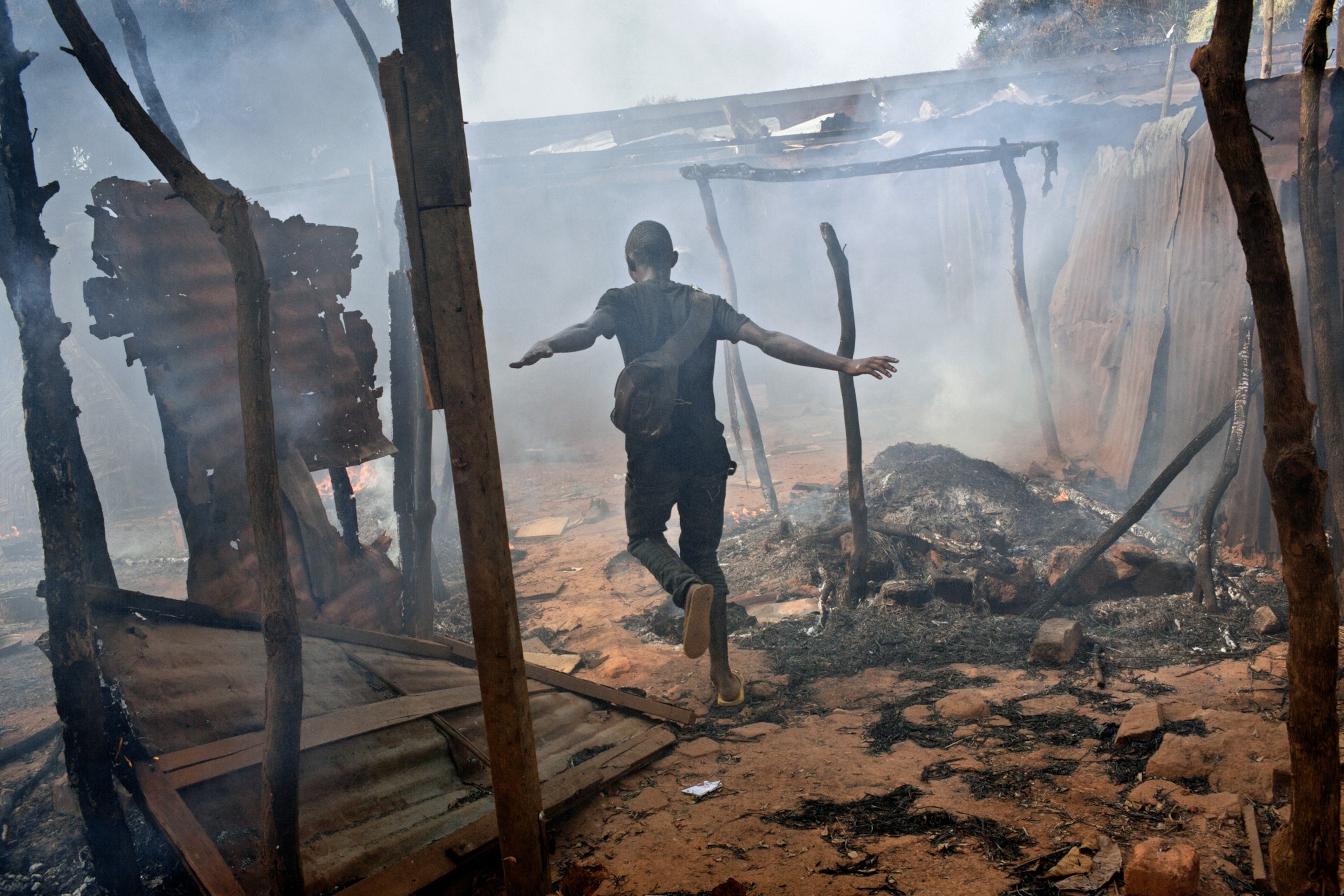 a young boy running through a structure burnt down by Christian led militia attacks