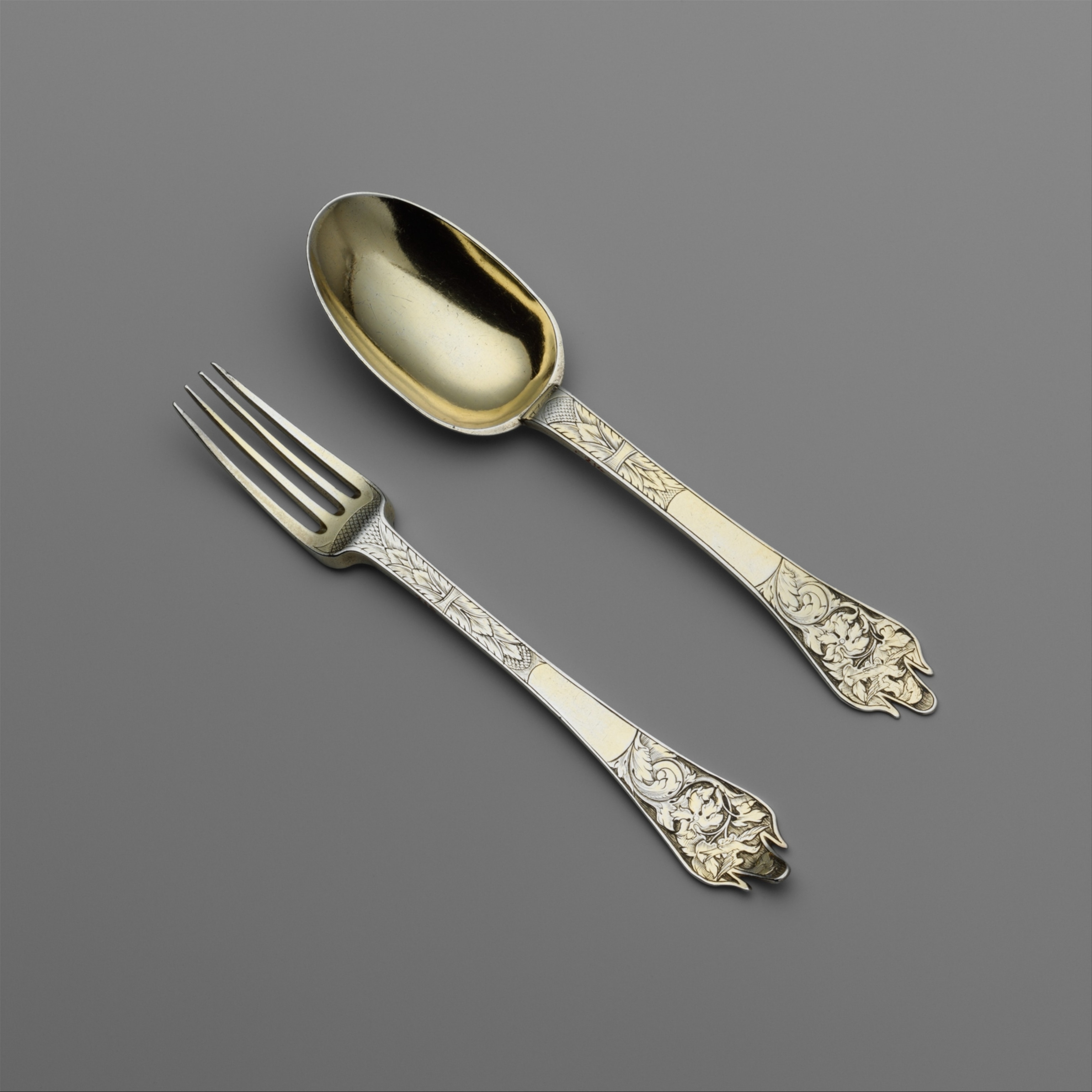 A fork and spoon with ornate details on the handles photographed on a grey background.