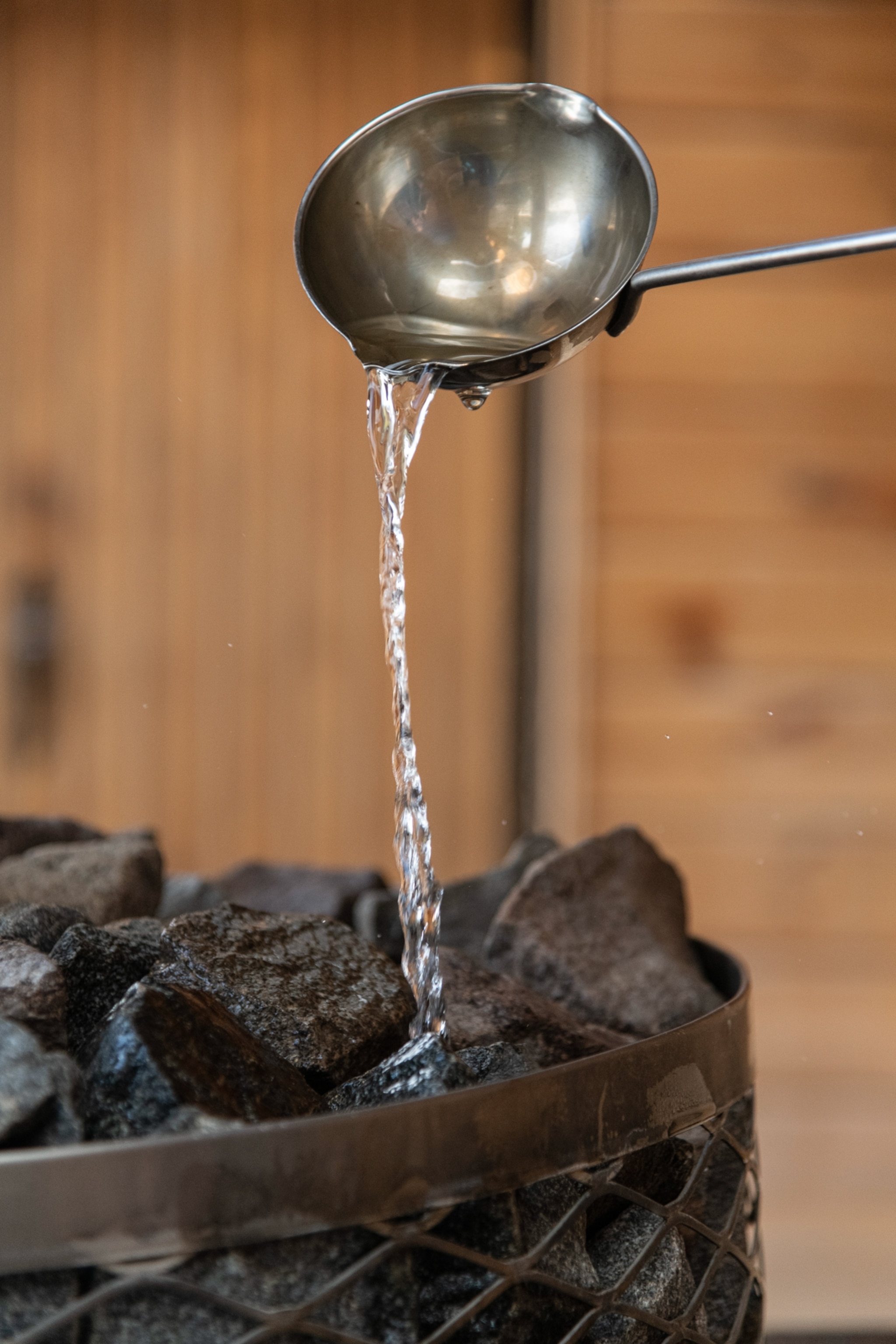 Water pouring from a ladle onto a basket of hot stones.