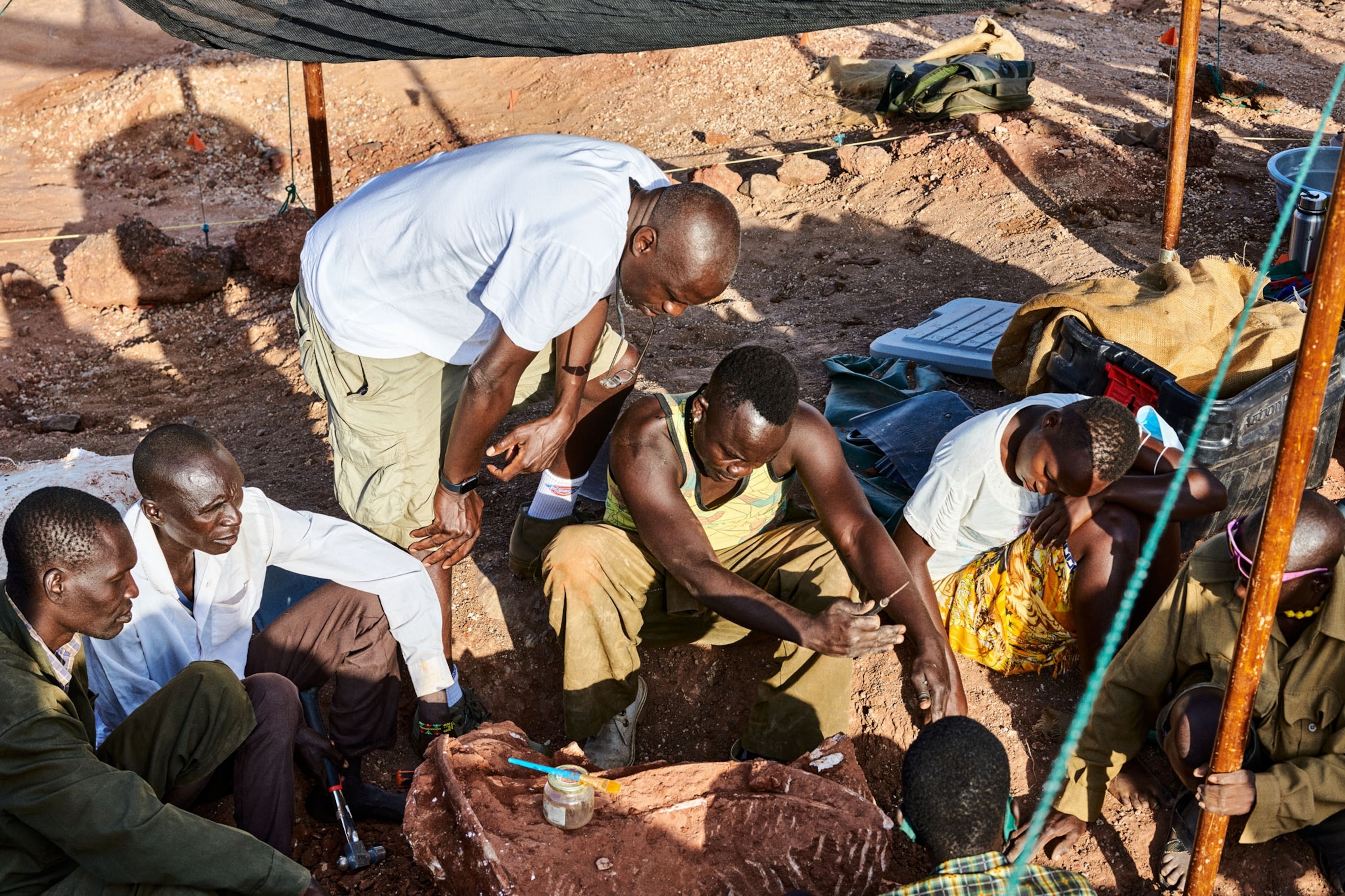 Picture of a man hovering over a seated group examining an object on the grond
