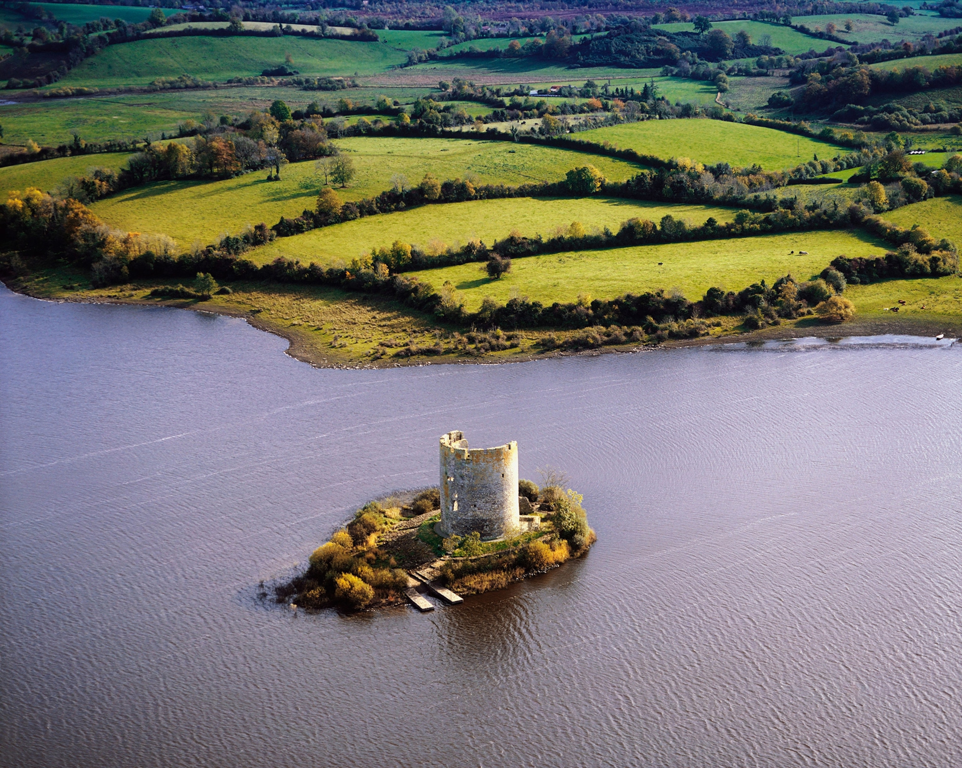 A castle sits on an island as with hills in the distance.