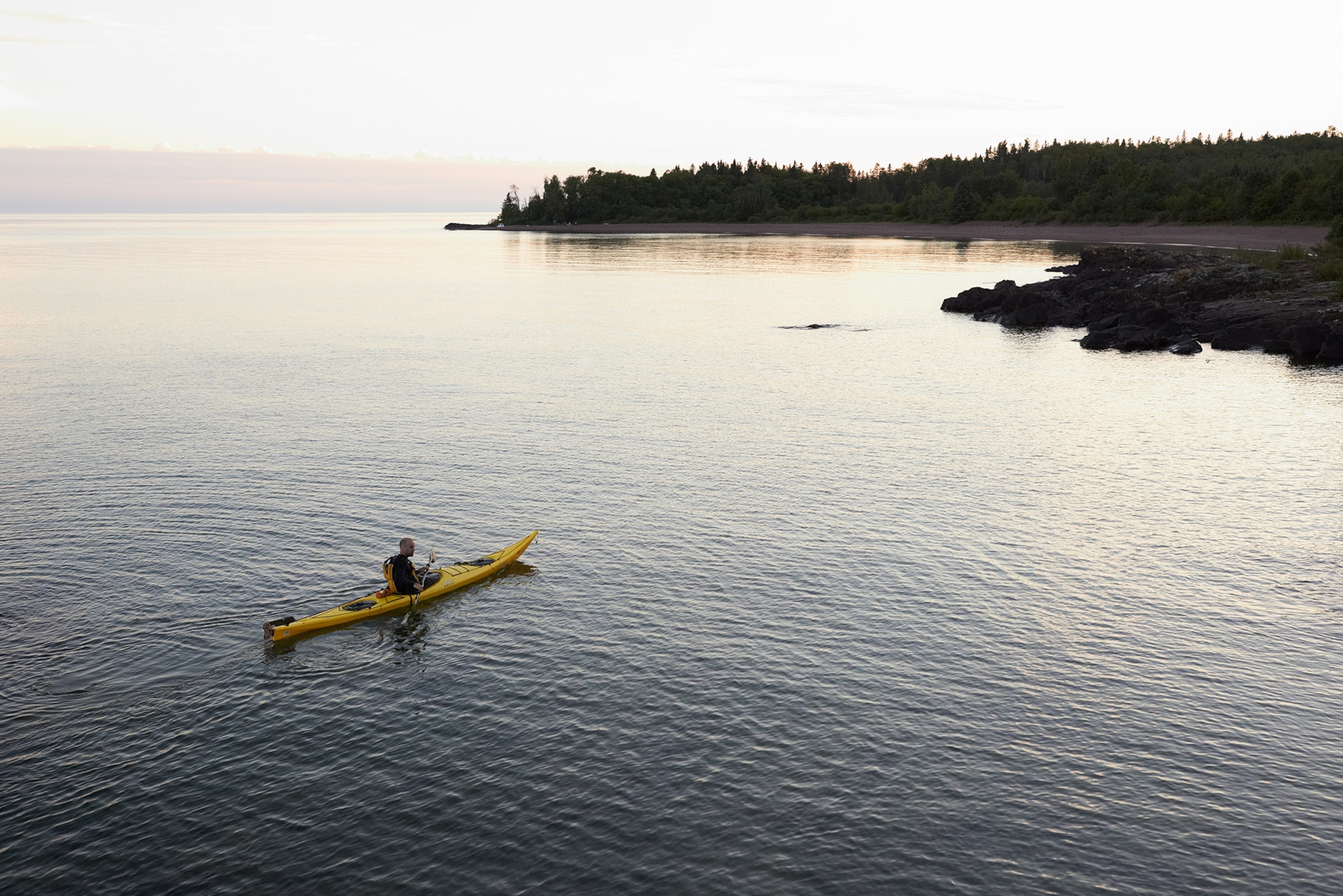 A man in a yellow kayak on lake.