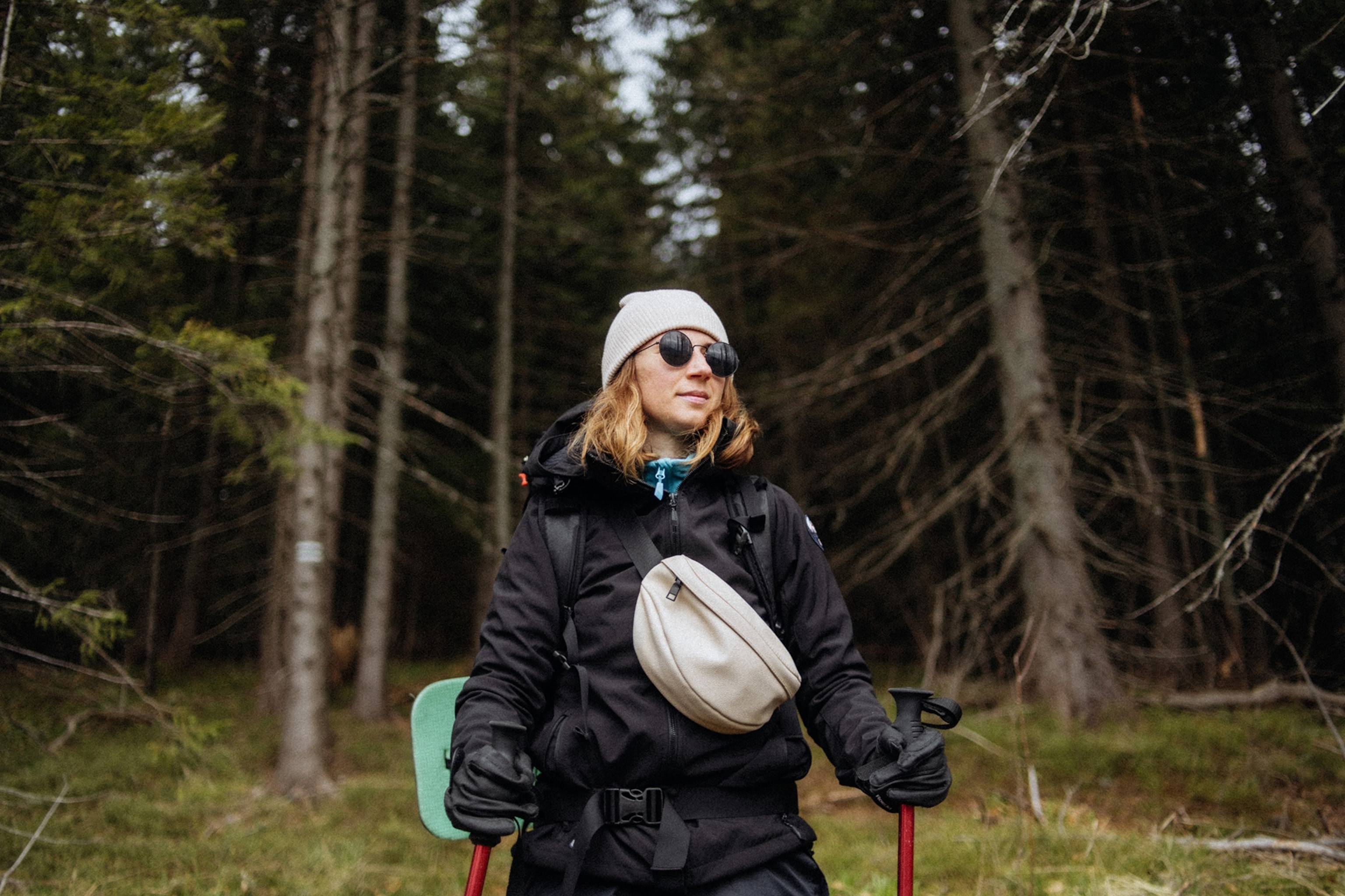 A woman with pale skin and blonde hair, black gloves, black jacket and outfit and white hat and black shades.