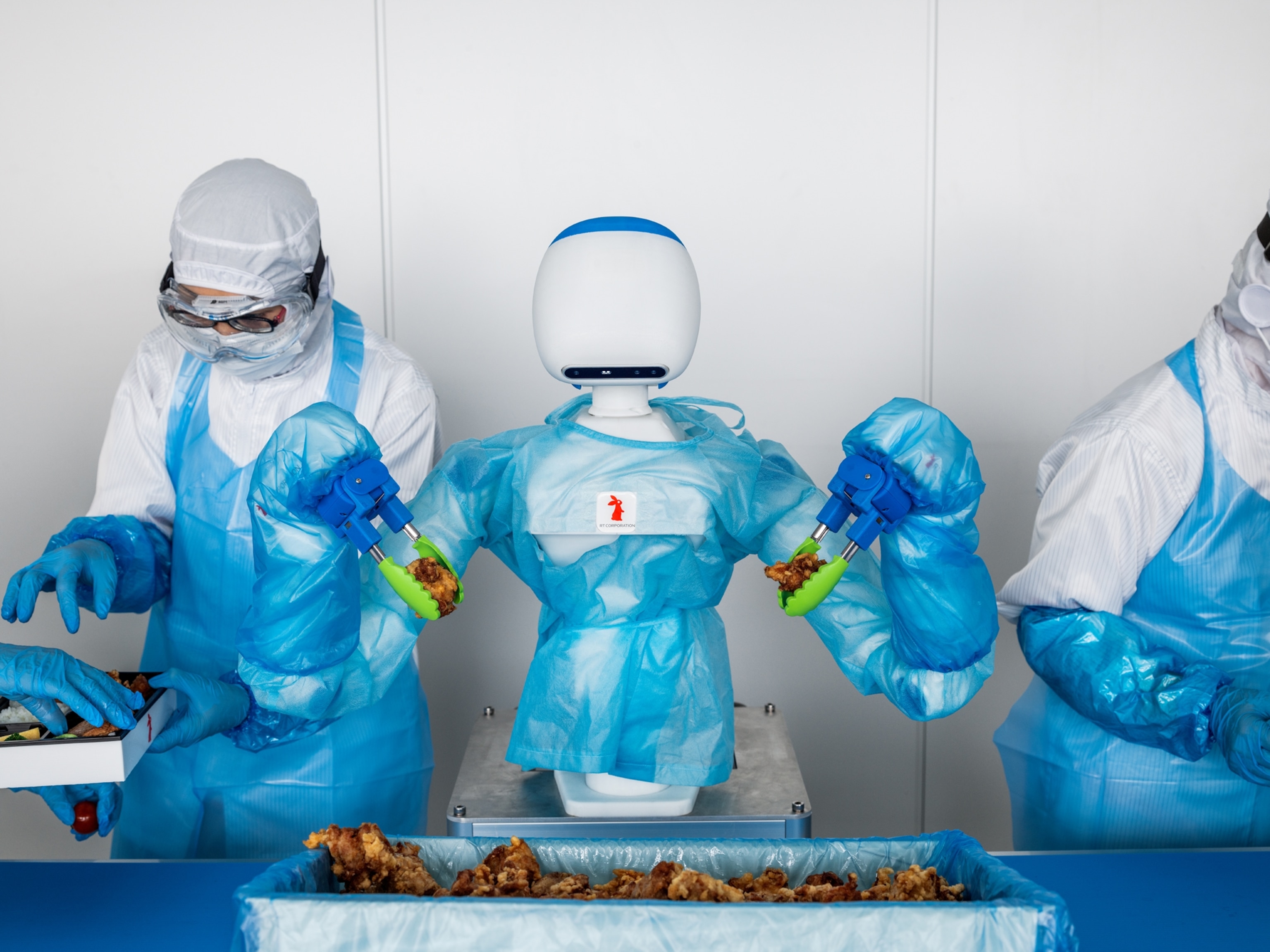 faceless robot in blue plastic apron packing fried chicken between two persons.