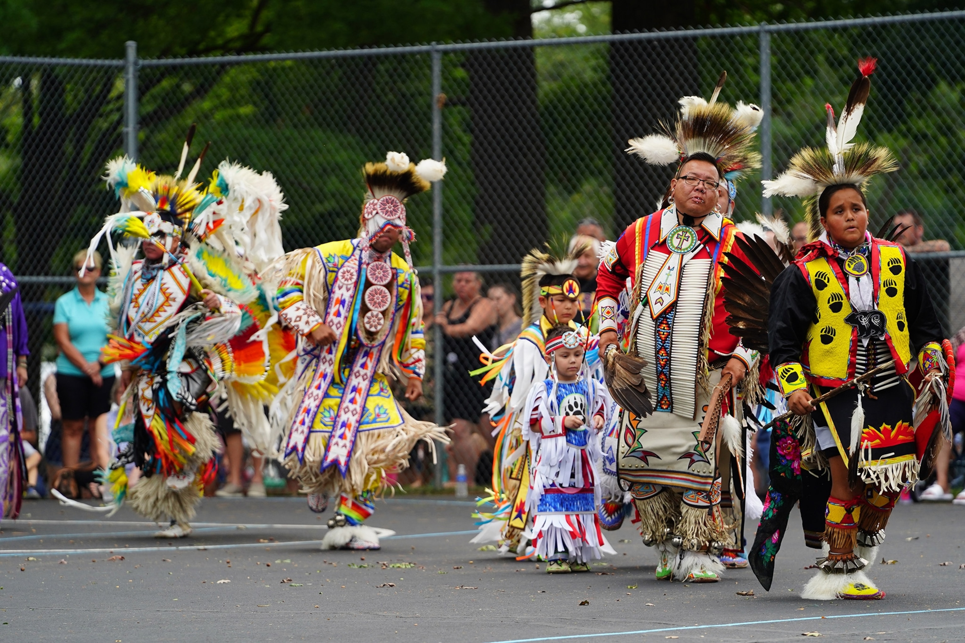 Dressed in colorful garbs people of various ages perform in front of spectators at a park.