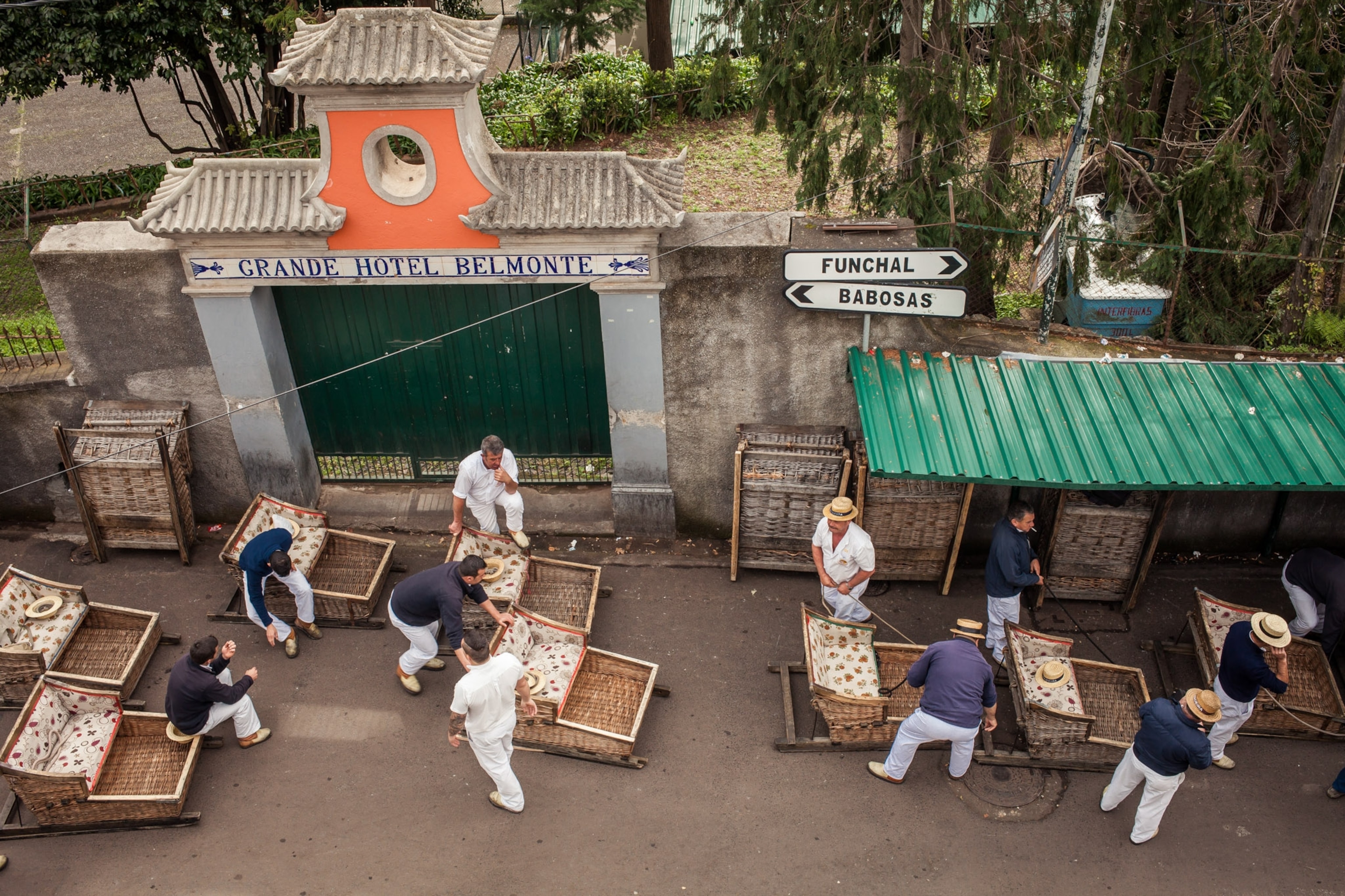 Men dressed in white stand outside of a hotel, with their baskets ready for travel.