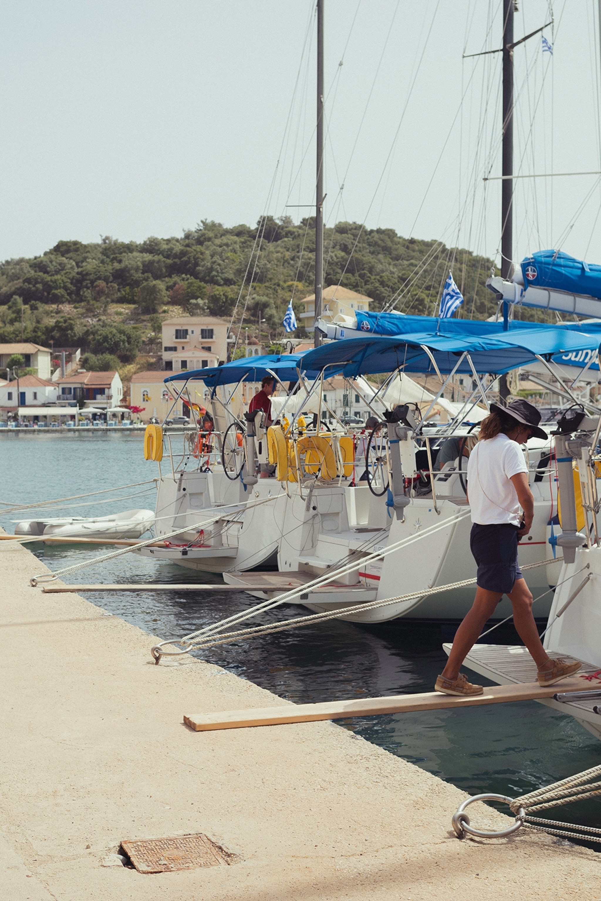 A man in skipper uniform walking on a wooden plank towards his boat that's one of many lined up in the harbour.