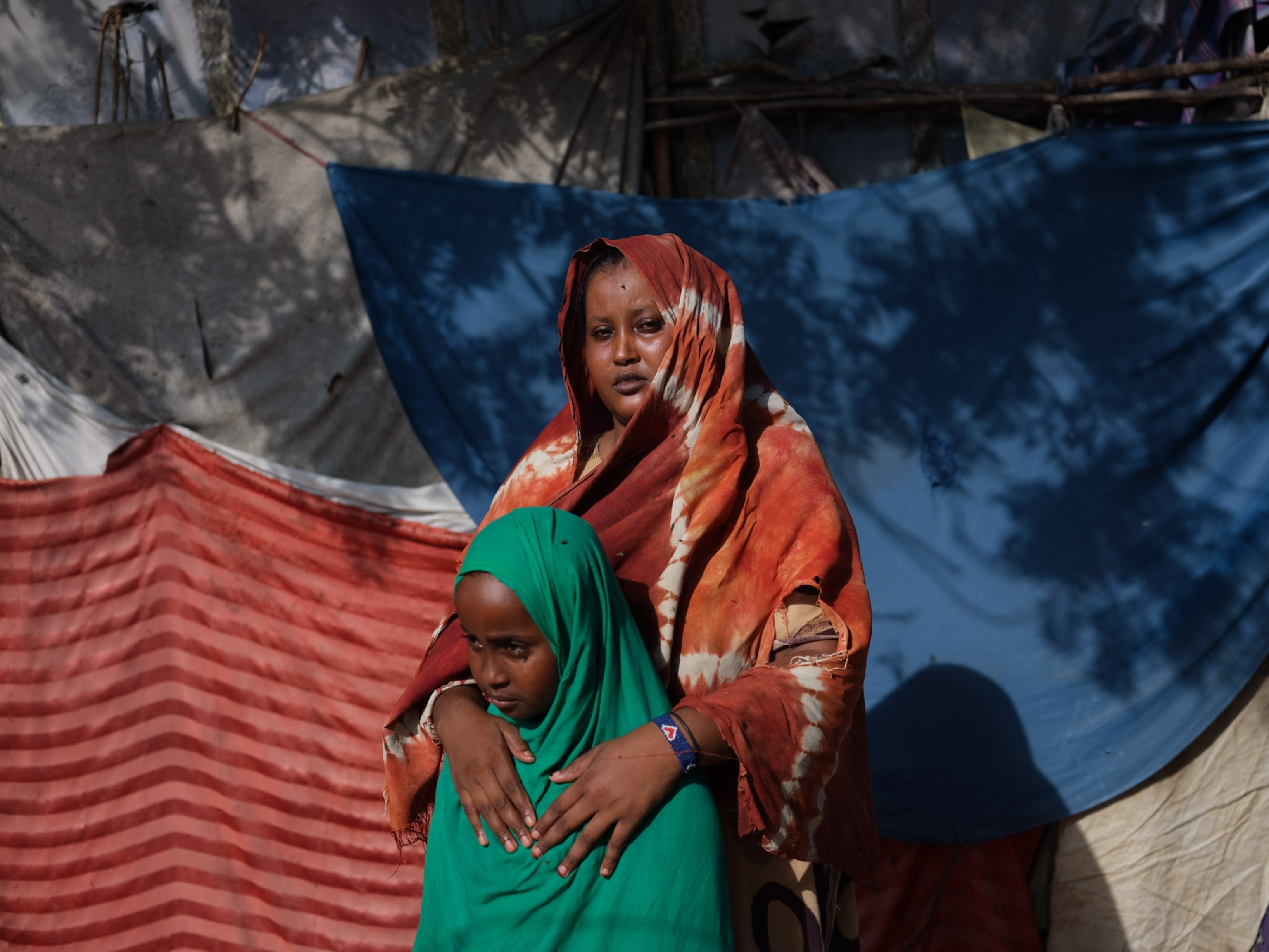 a mother in an orange scarf with her hands on shoulders of a young woman in a green scarf