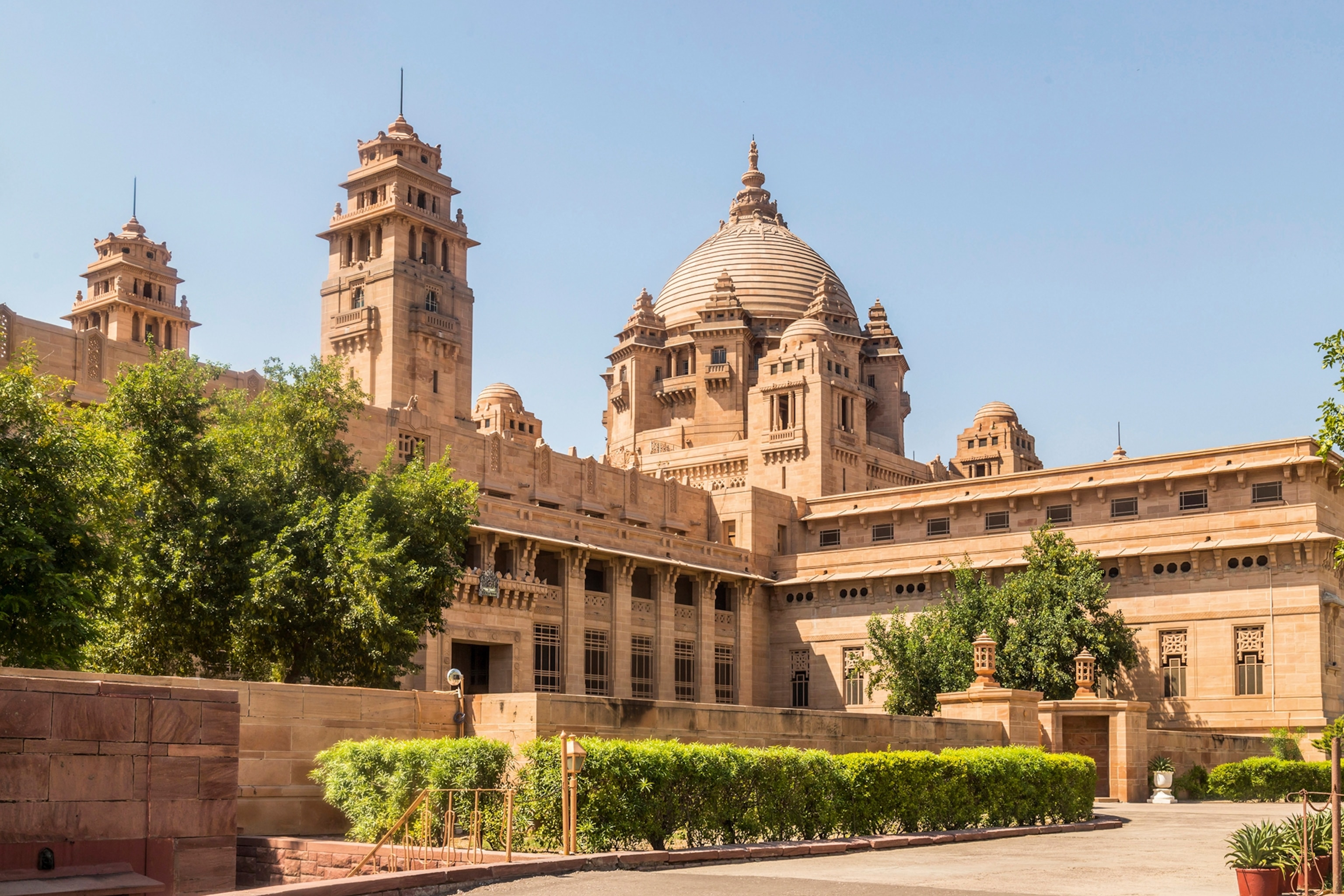 Sandstone palace with windows and a dome surrounded by green trees