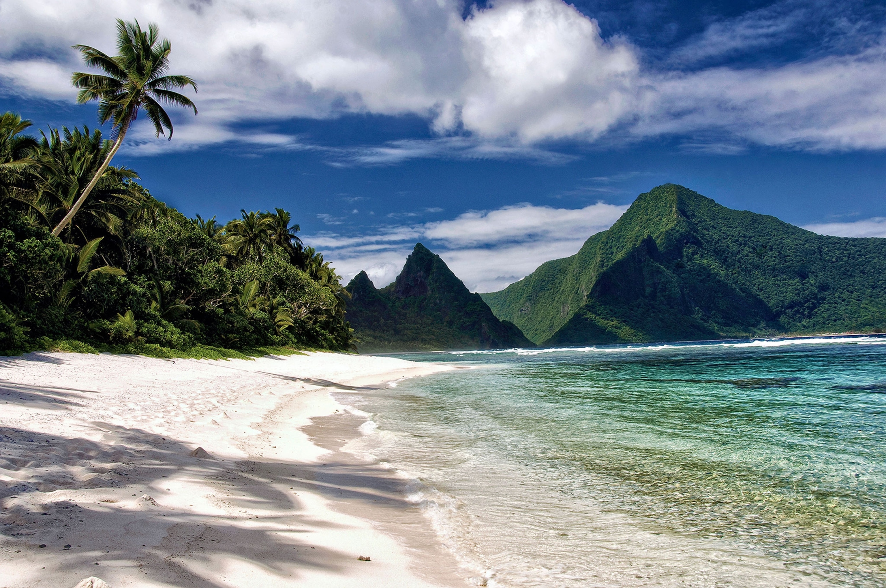 A secluded tropical sand beach and fringing reef in the Samoa National Park in Ofu Island, American Samoa. The island of Olosega rises in the distance.