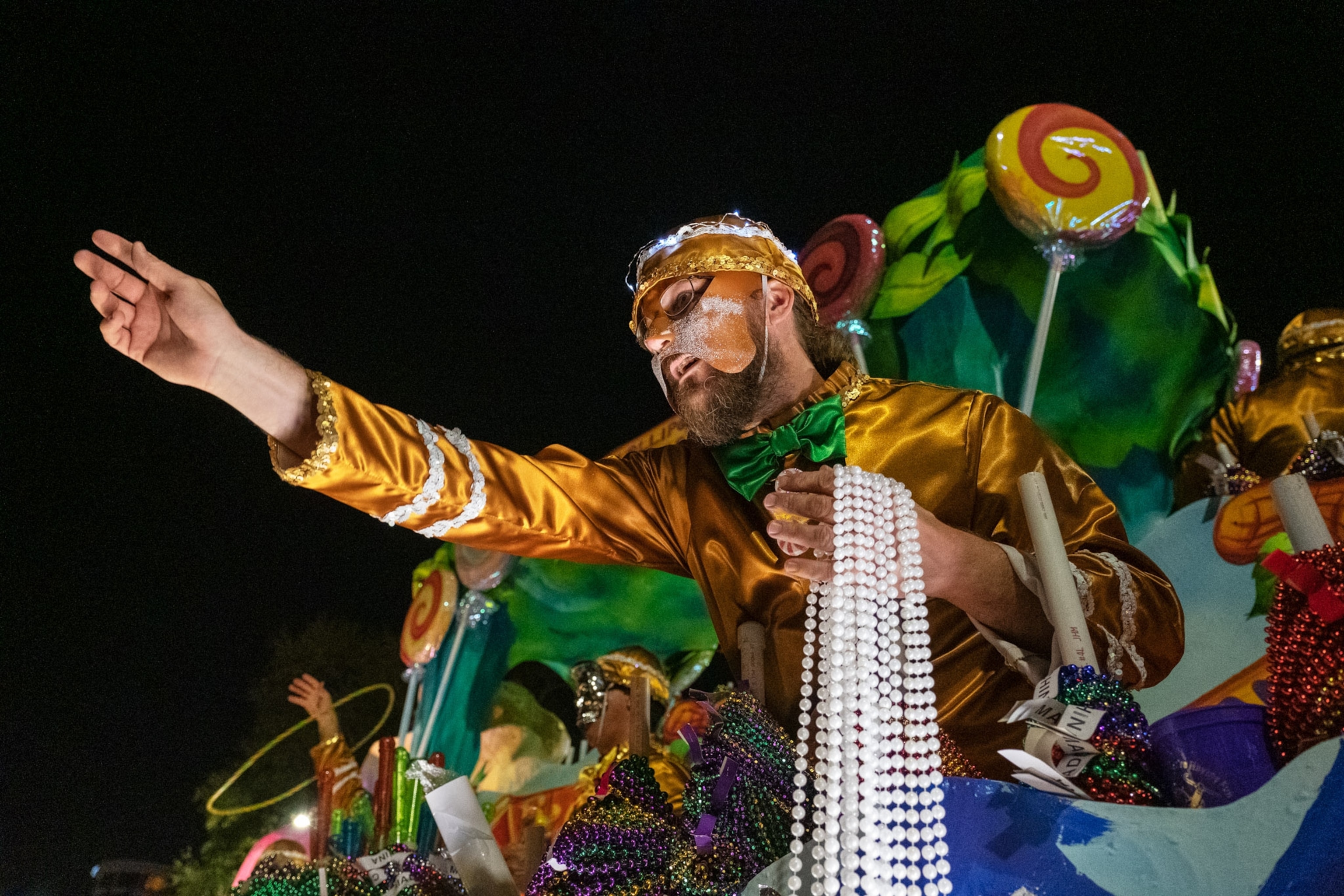 a person holding beads leaning over a Mardi Gras float
