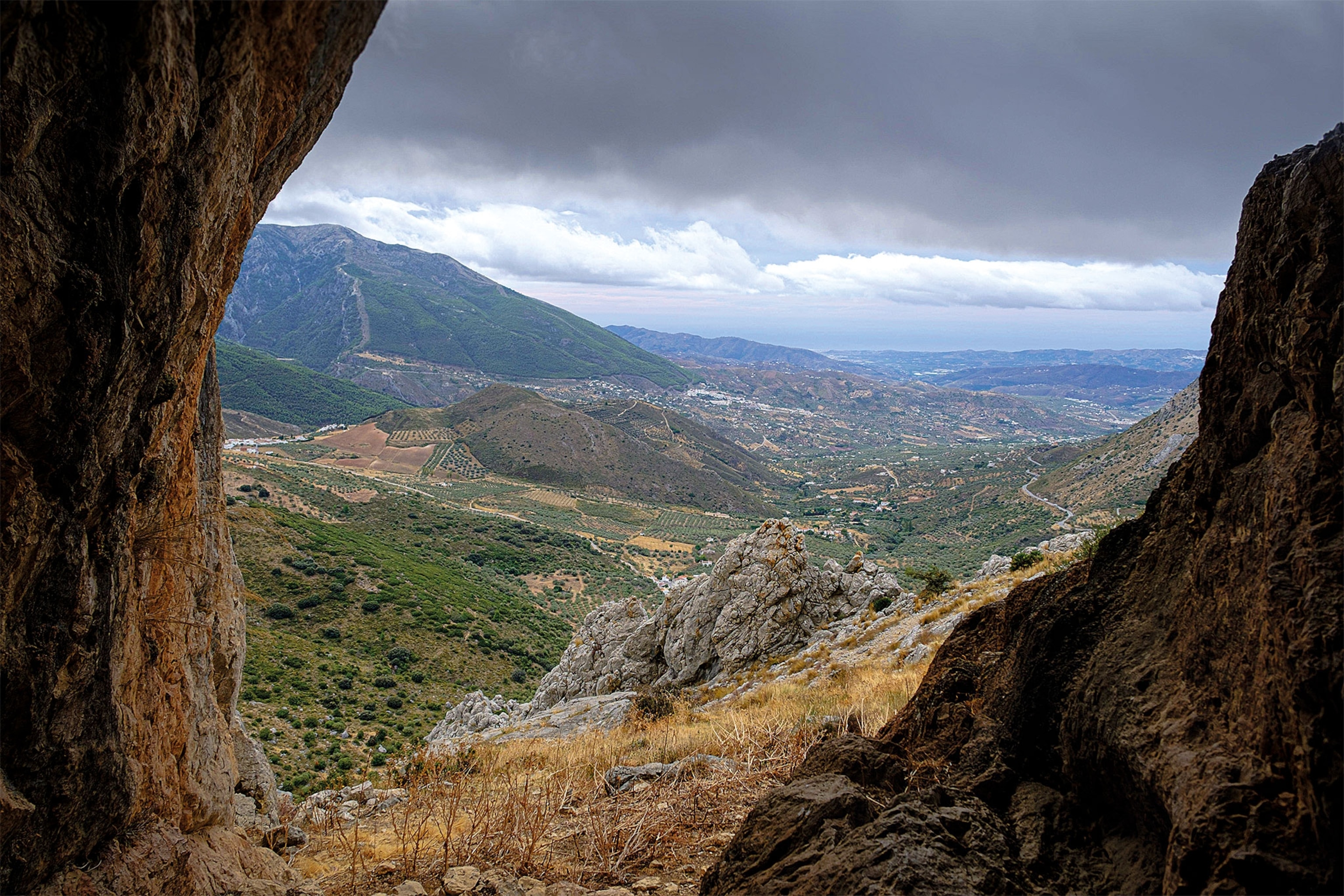 A view of mountains and houses from the opening of a cave
