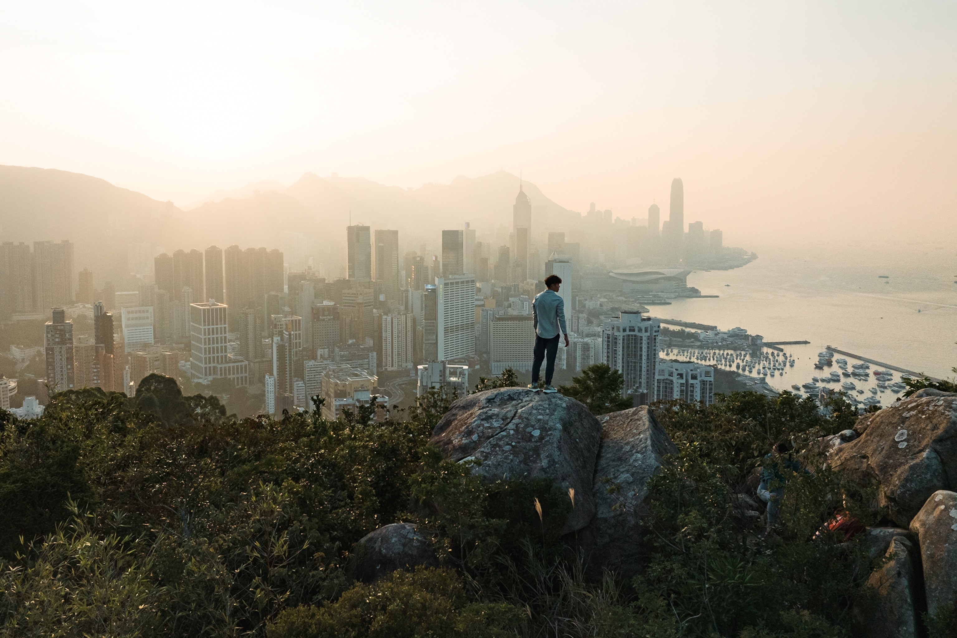 A man standing on the edge of a cliff overlooking the Hong Kong city and coastline.