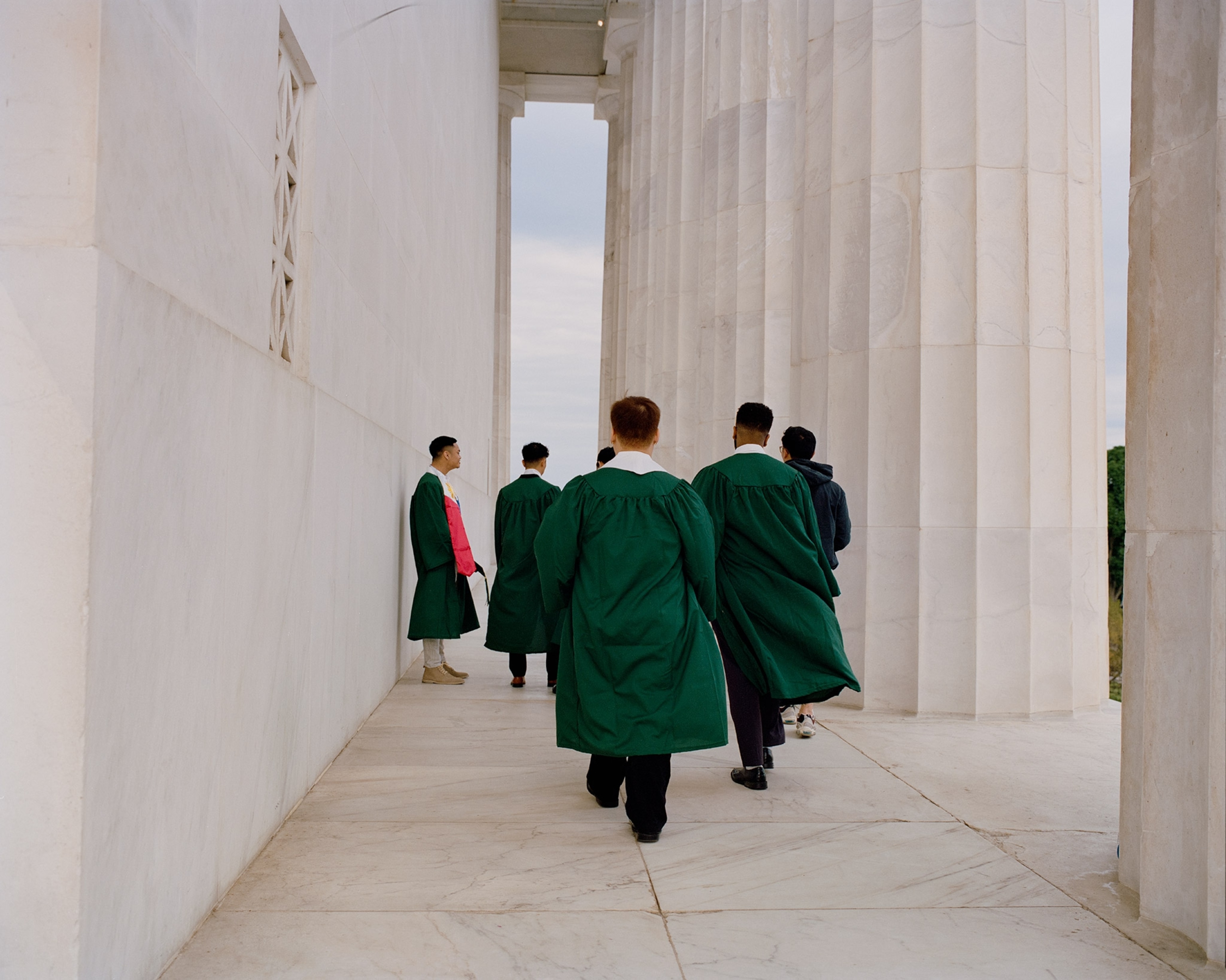 Graduates walk in green caps and gowns along the steps of the Lincoln Memorial in Washington D.C.