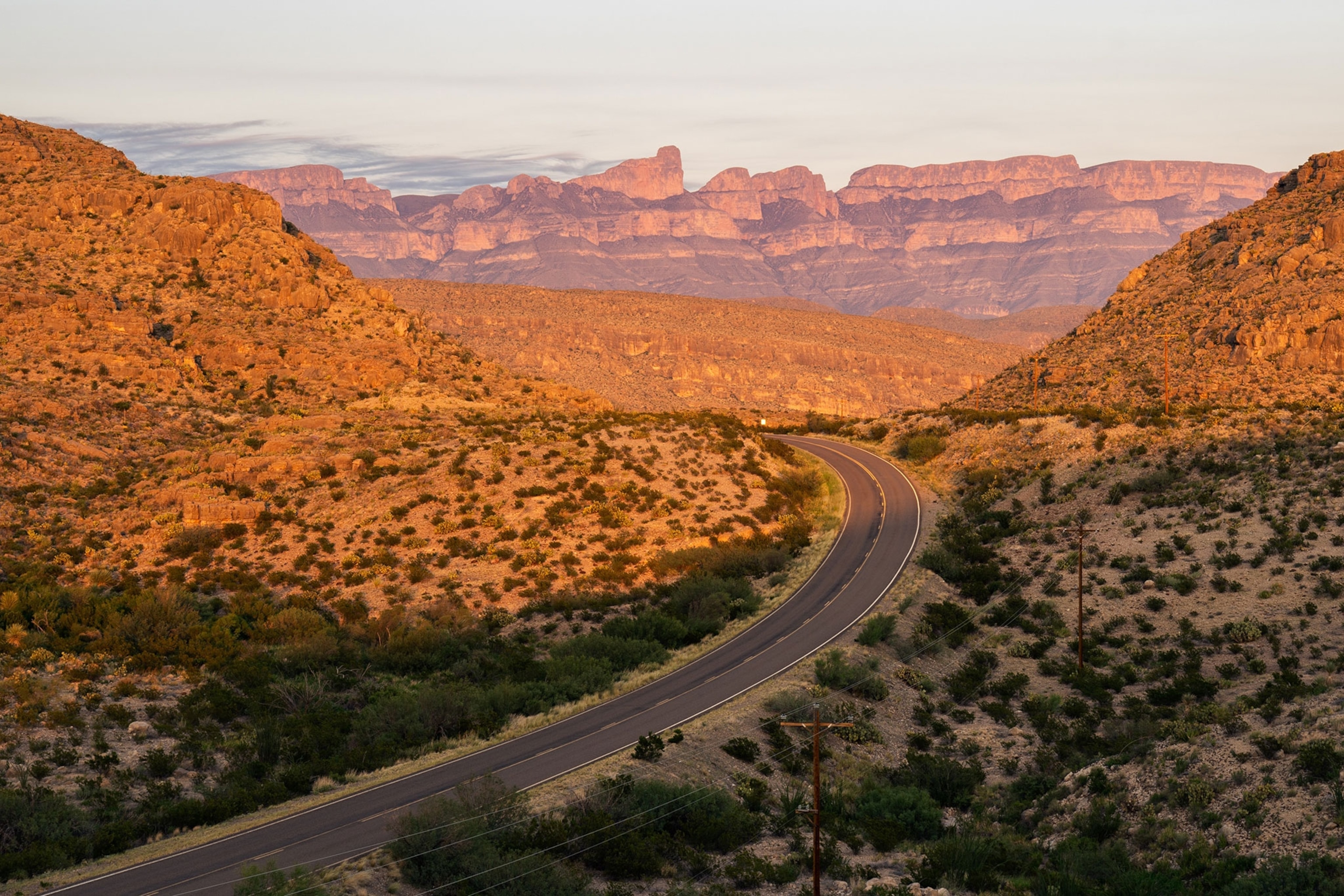 Landscape of a desert with a road in the valley of mountains curving through the center of the frame.