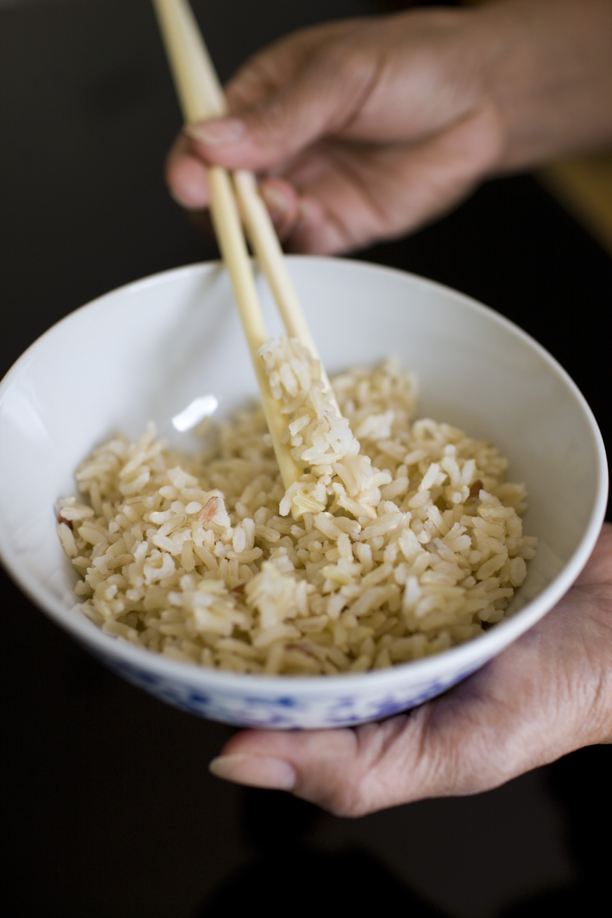 A close-up view of a woman holding a bowl of cooked brown rice.