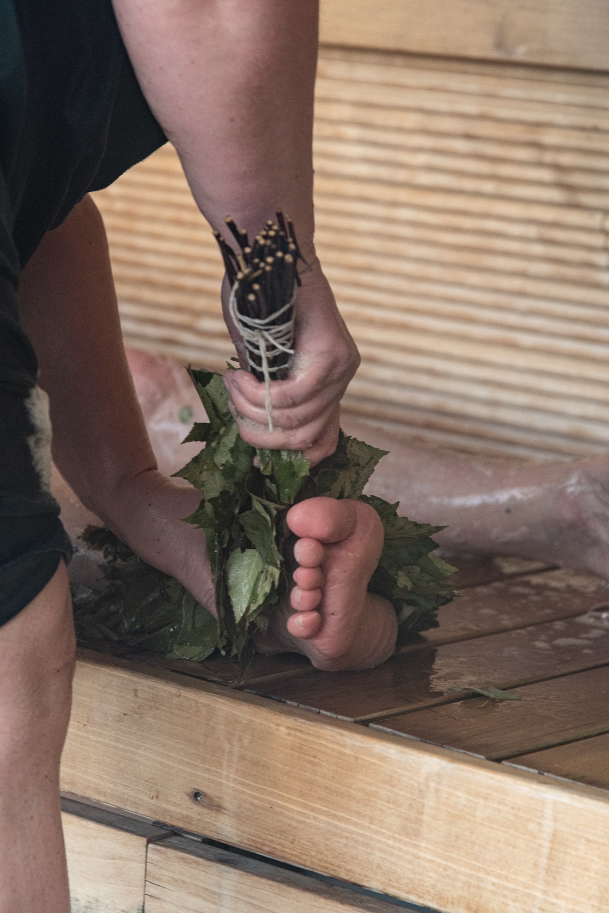 A woman using a birch whisk to scrub her legs and feet.