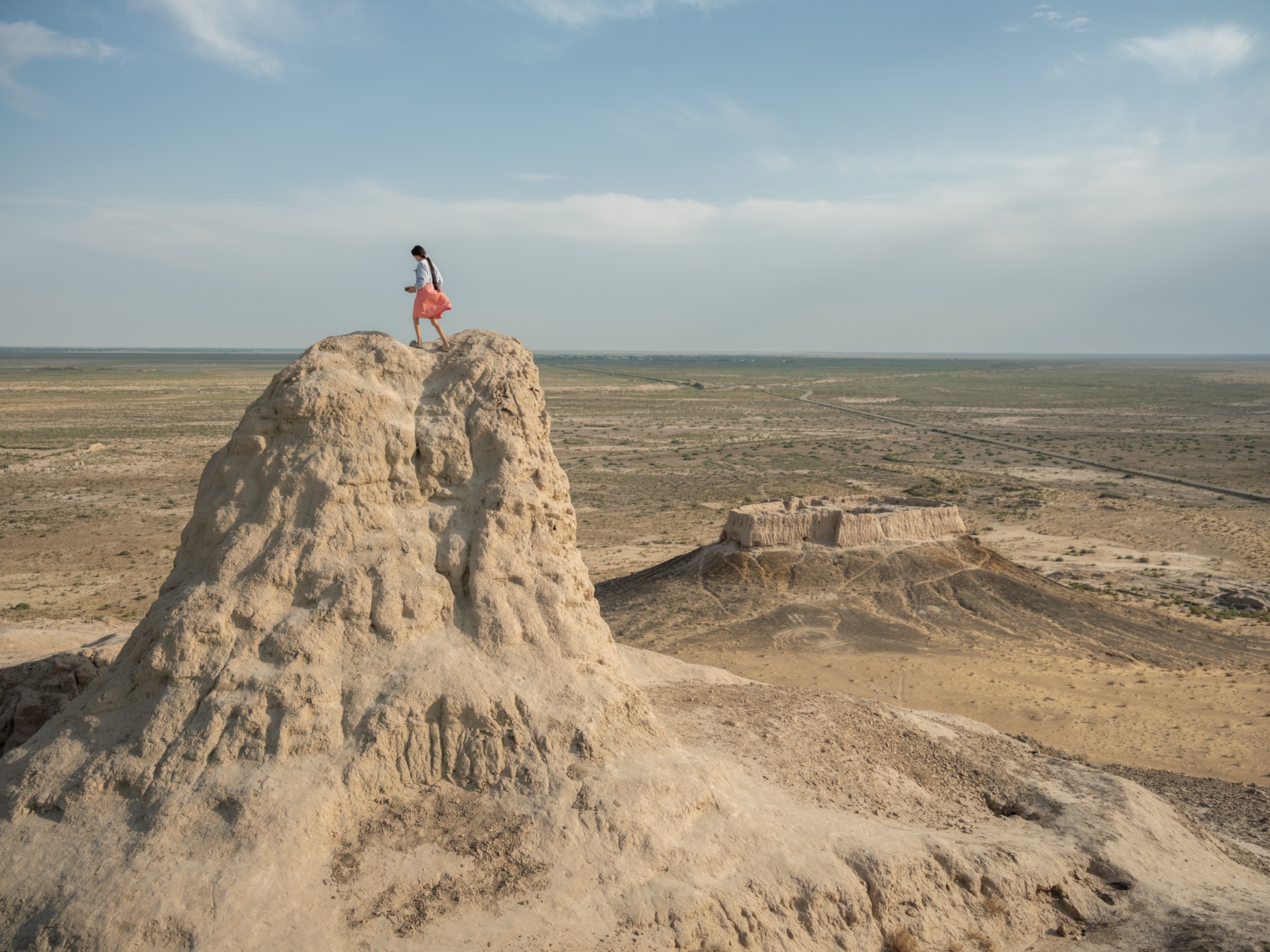 A young girl is standing on top of an eroded citadel, with an arid landscape behind her.