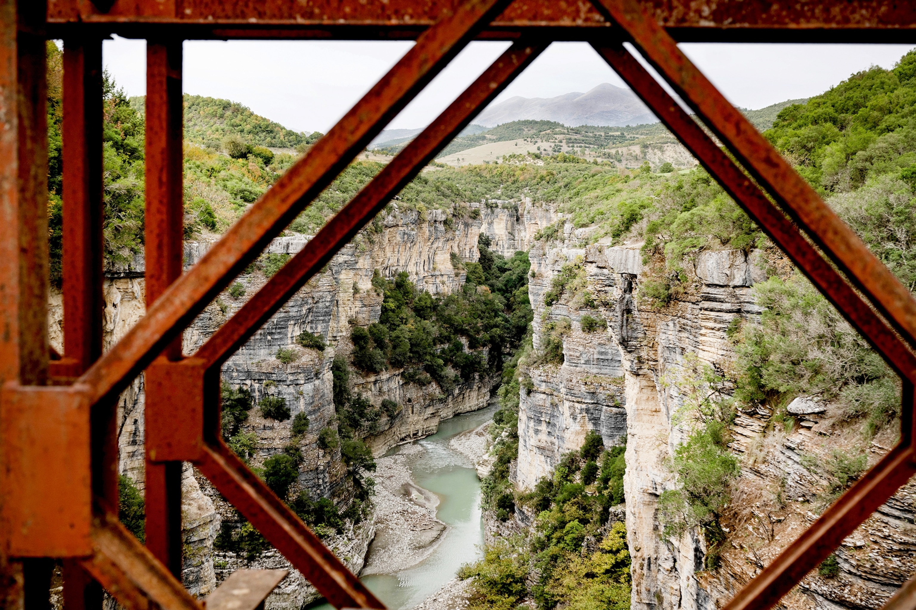 A view through a red grill to the Osumi canyon in Albania which has a body of light blue water running through it.