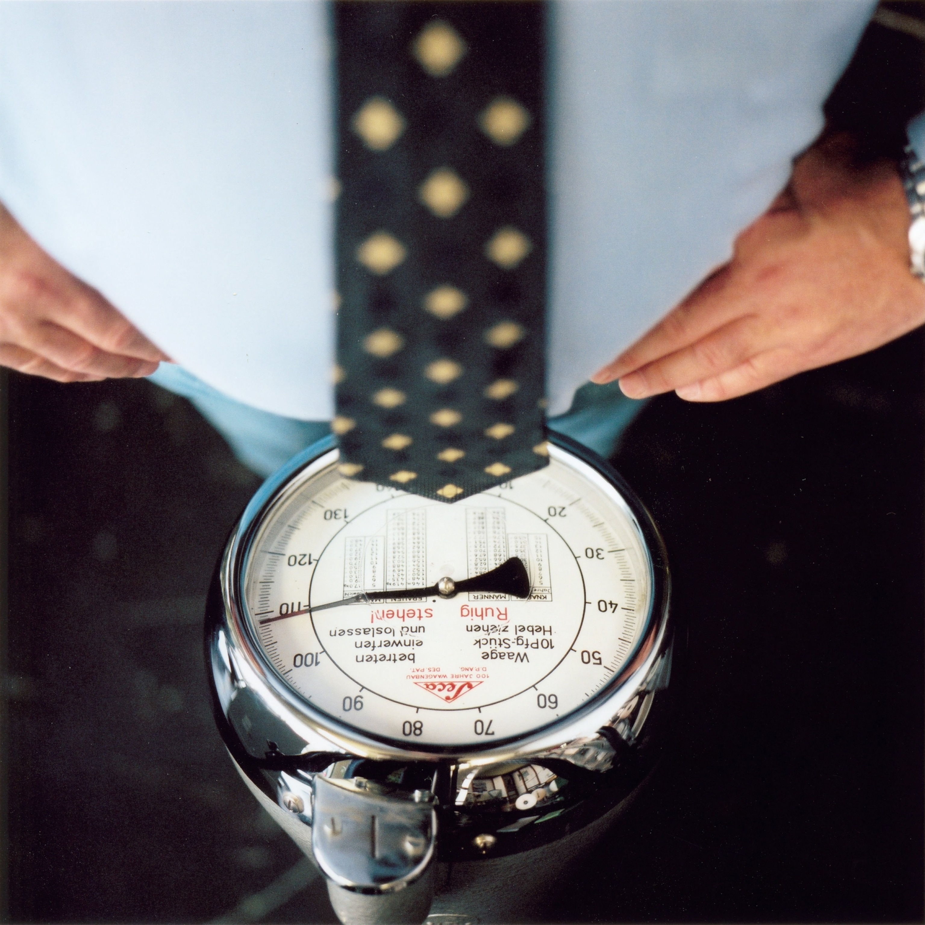 A scale nearing 109 Kg is seen beneath the belly of an obese man.