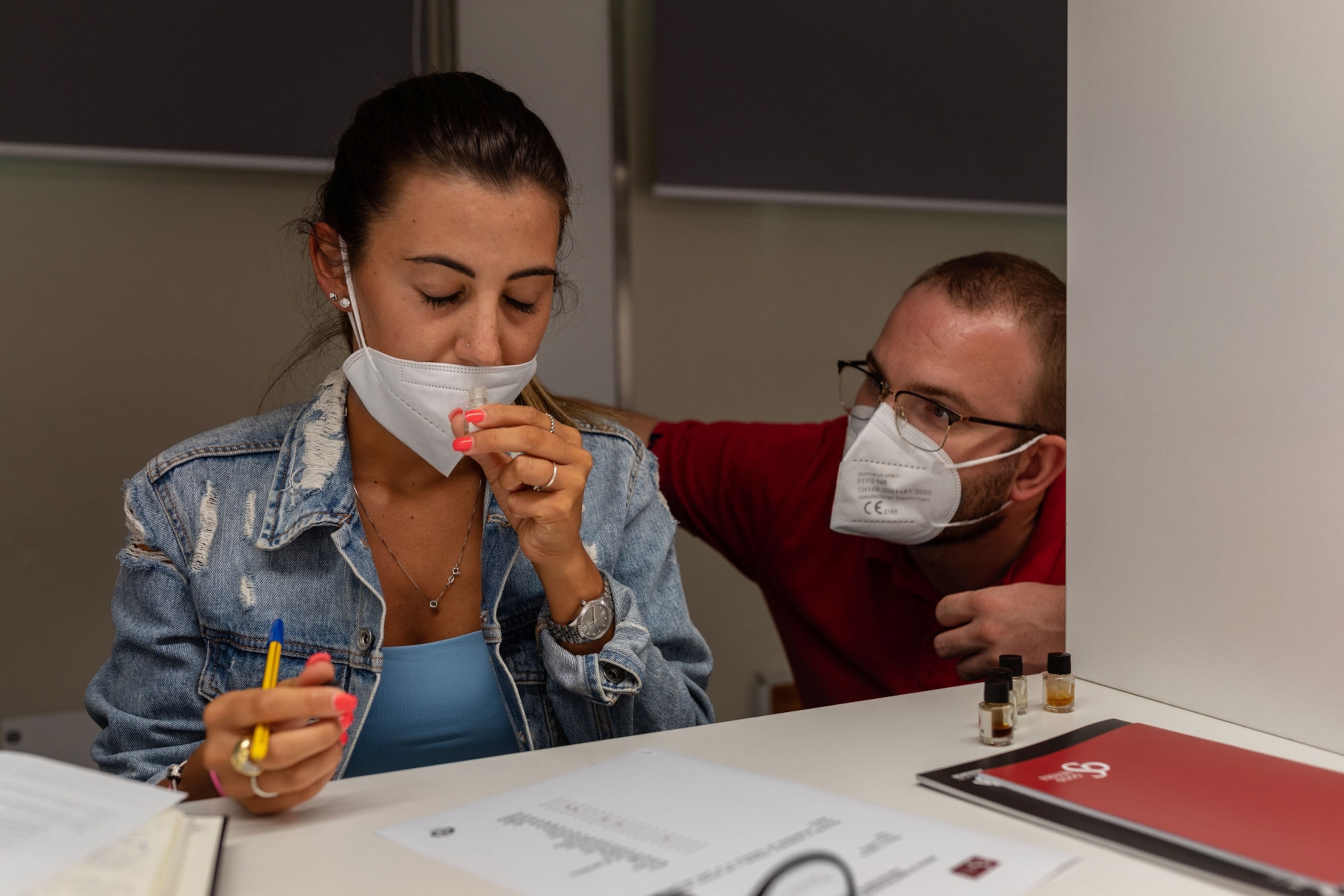 A woman sniffs a vial while wearing a mask