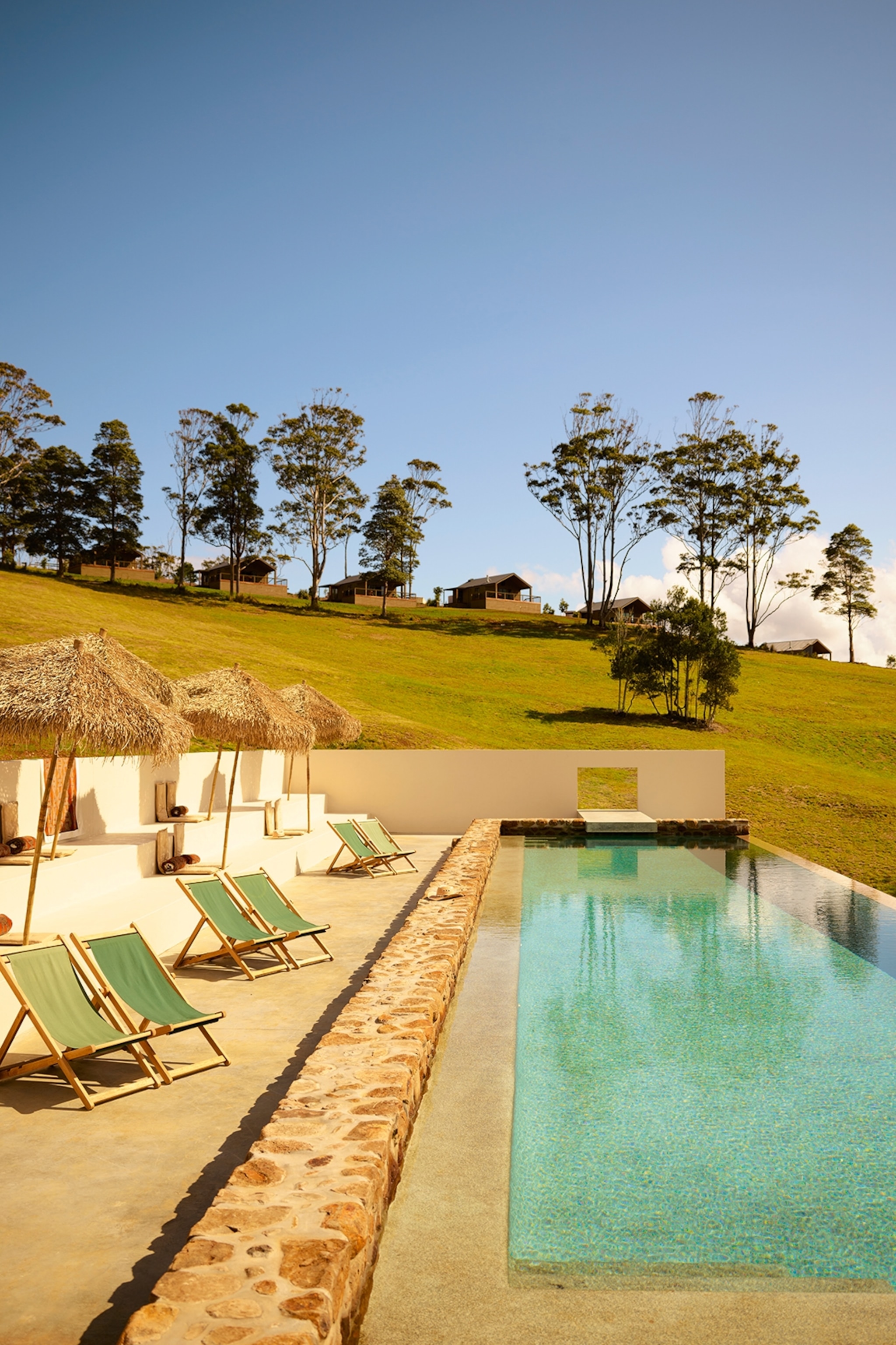Infinity pool on a hillside with deckchairs and straw umbrellas positioned alongside