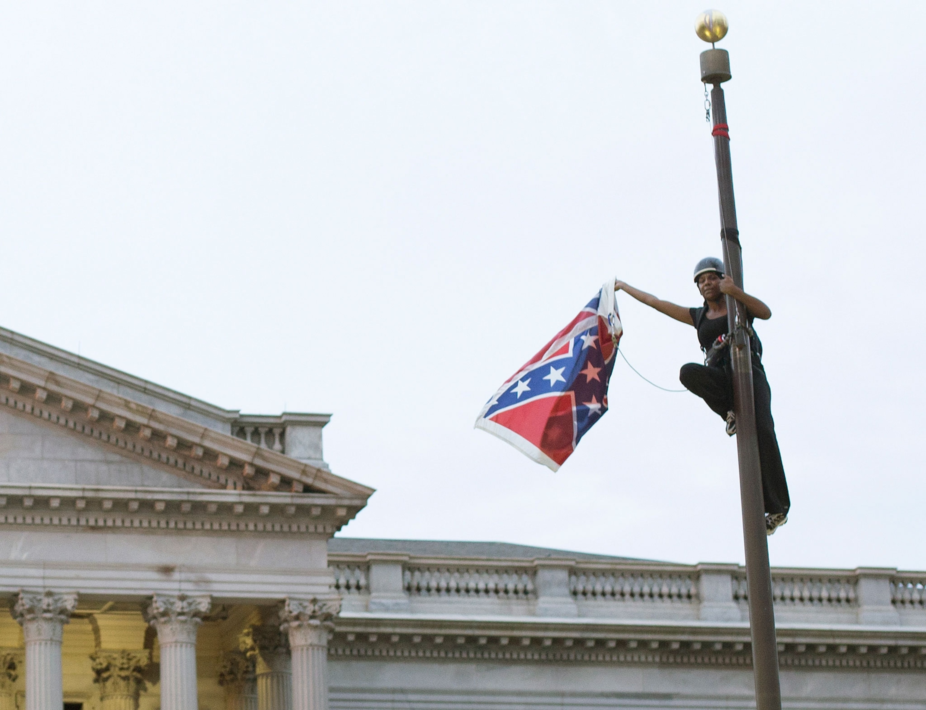 A woman on a flagpole removes a confederate flag