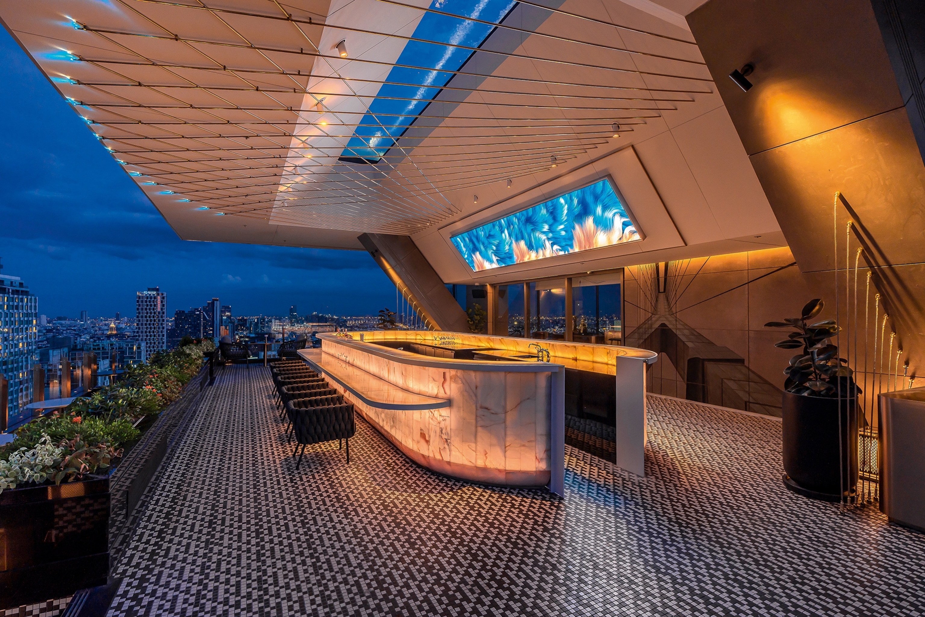 Grand hotel outdoor bar with tiled floor overlooking a city skyline at night with glimmering lights