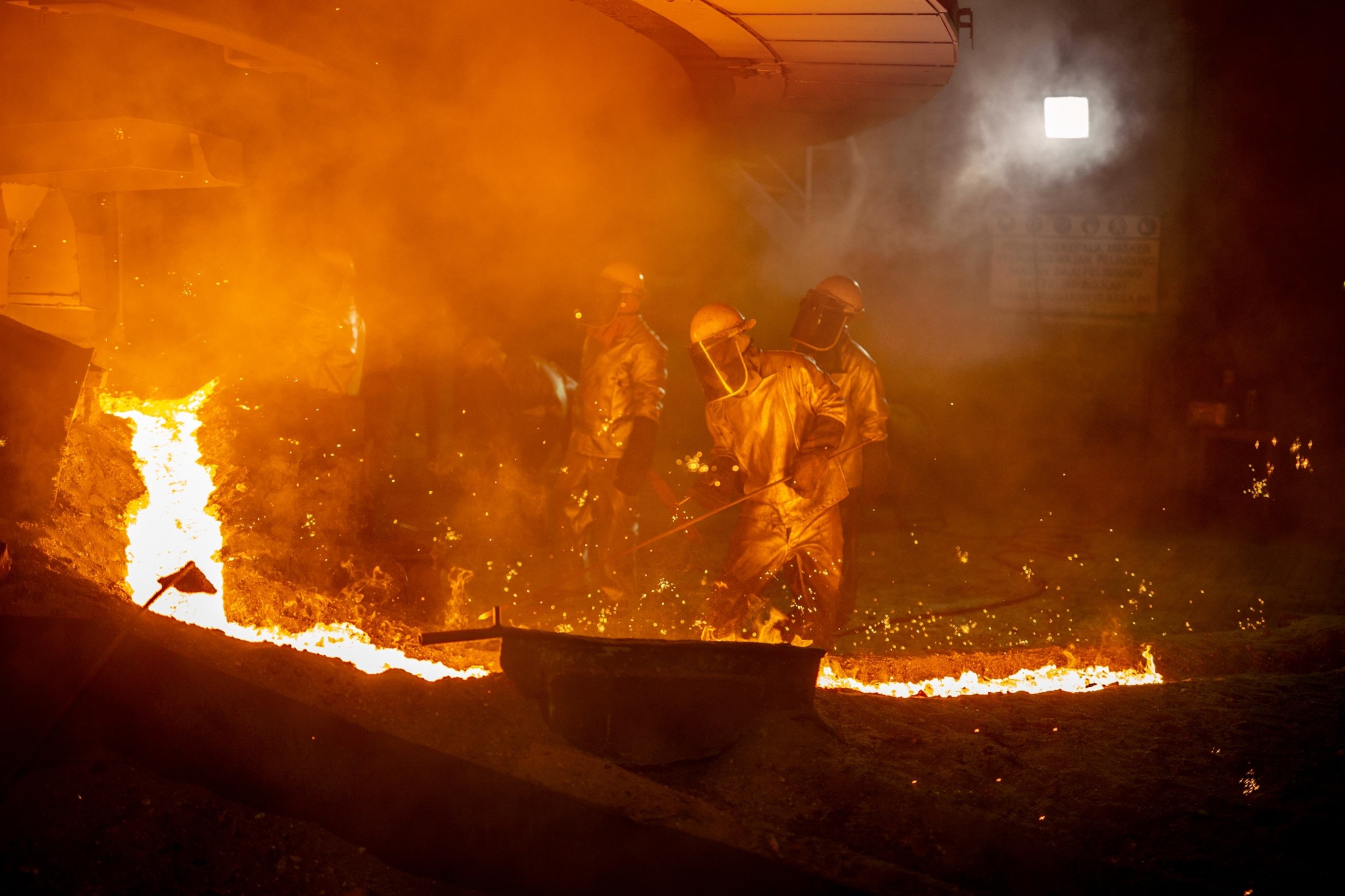 Picture of workers in fire-proof coverups next to stream of melted metal.