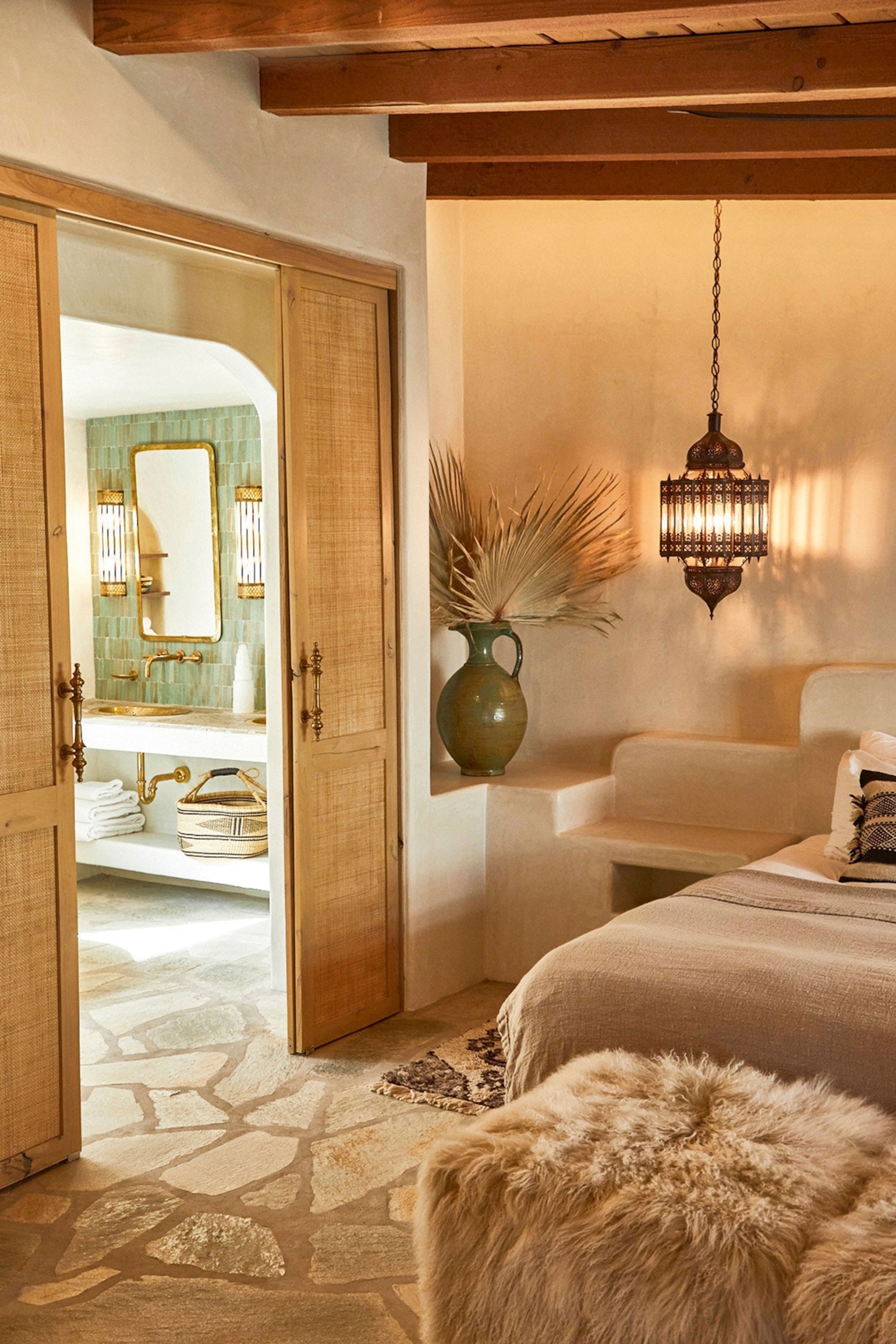 Hotel bedroom with neutral colours and doors opening to a bathroom with green tiles