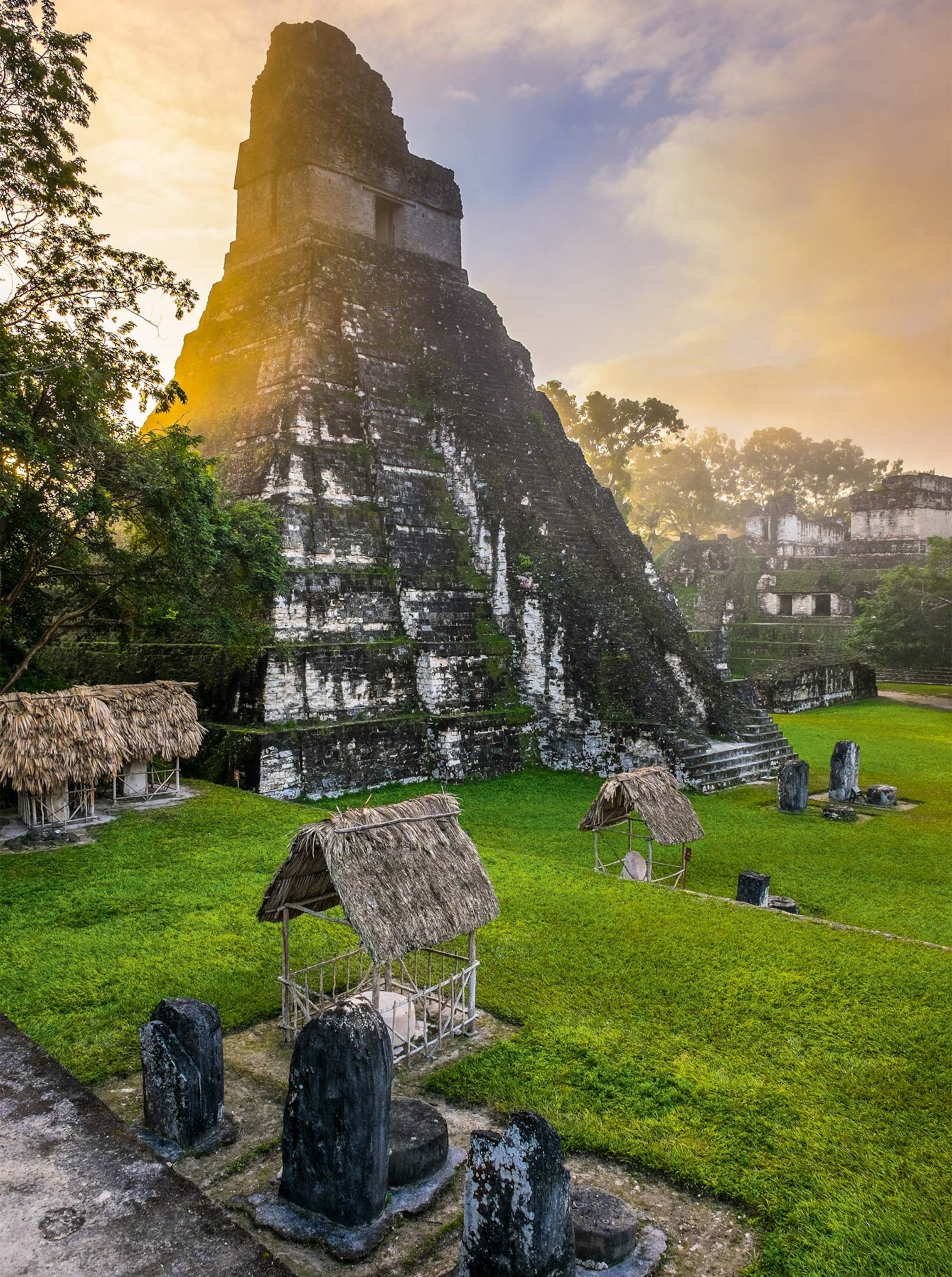 A pyramid among the ruins in the Great Plaza of Tikal, with the sun shining behind it