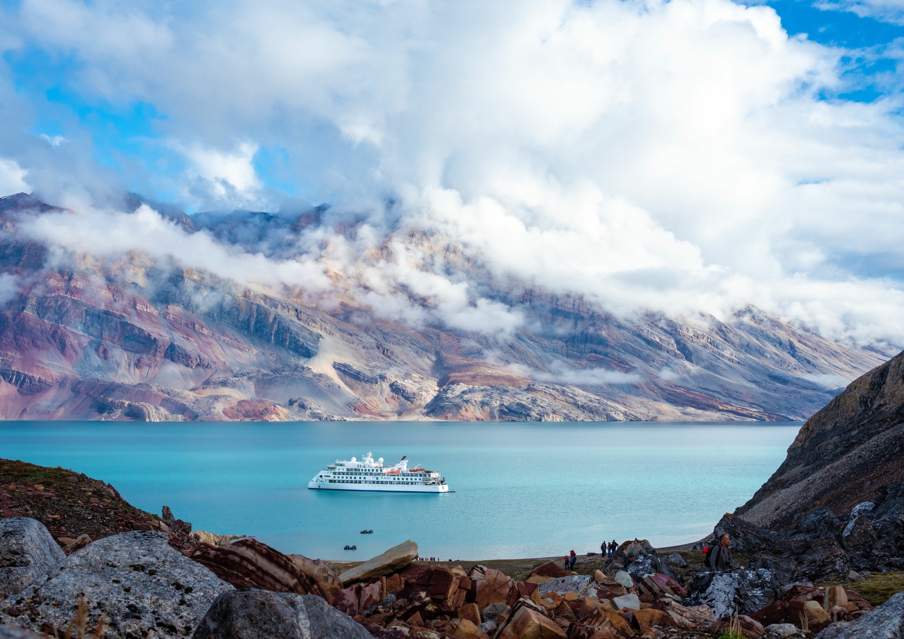 The Greg Mortimer cruise ship sailing in Greenland. It is white, and the water is a rich blue.