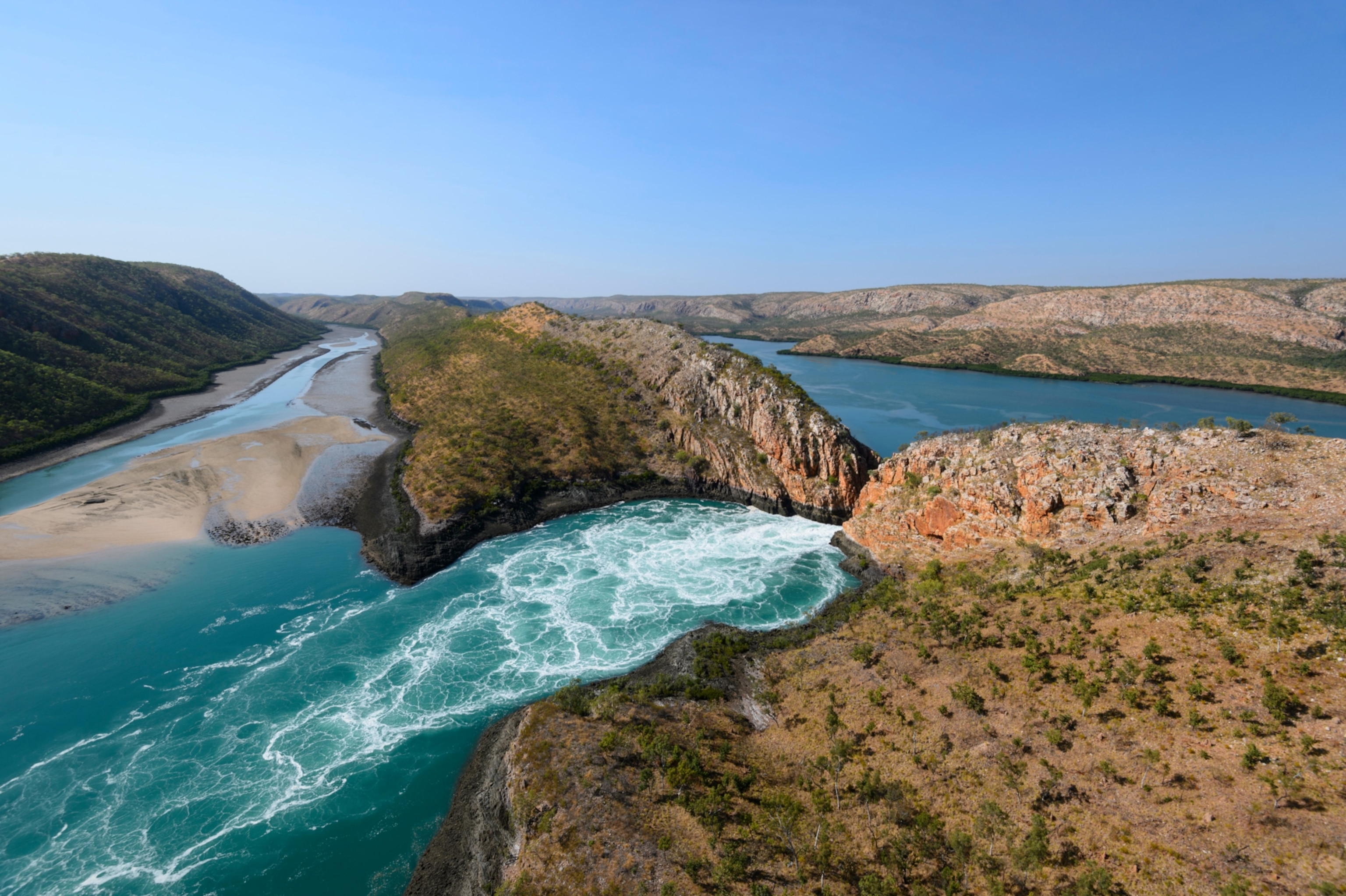 Water rushes between two bodies of land, creating waterfall like ripples on the water's surface
