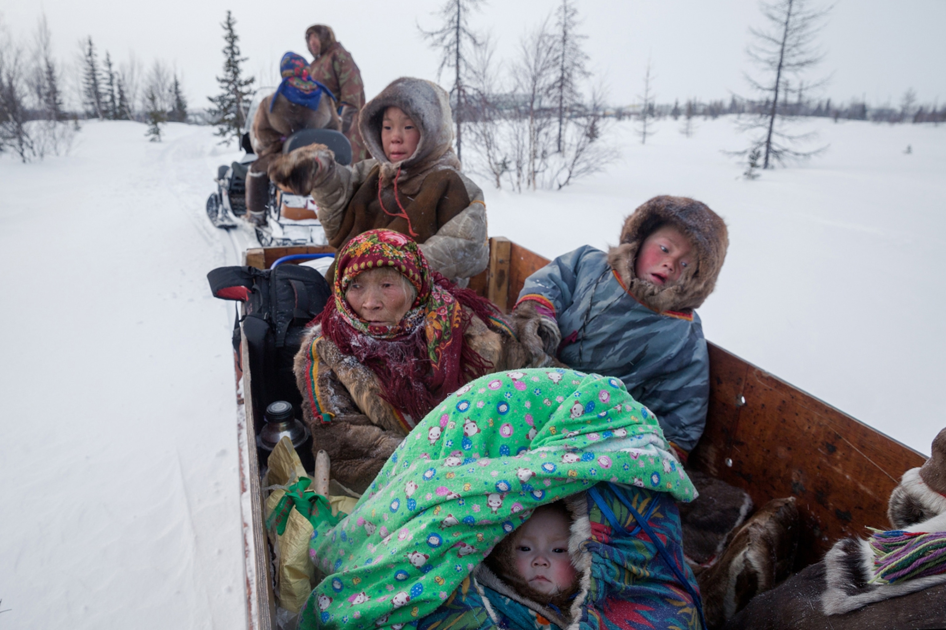 a grandmother in a wooden sleigh with three children in colorful and furry coats