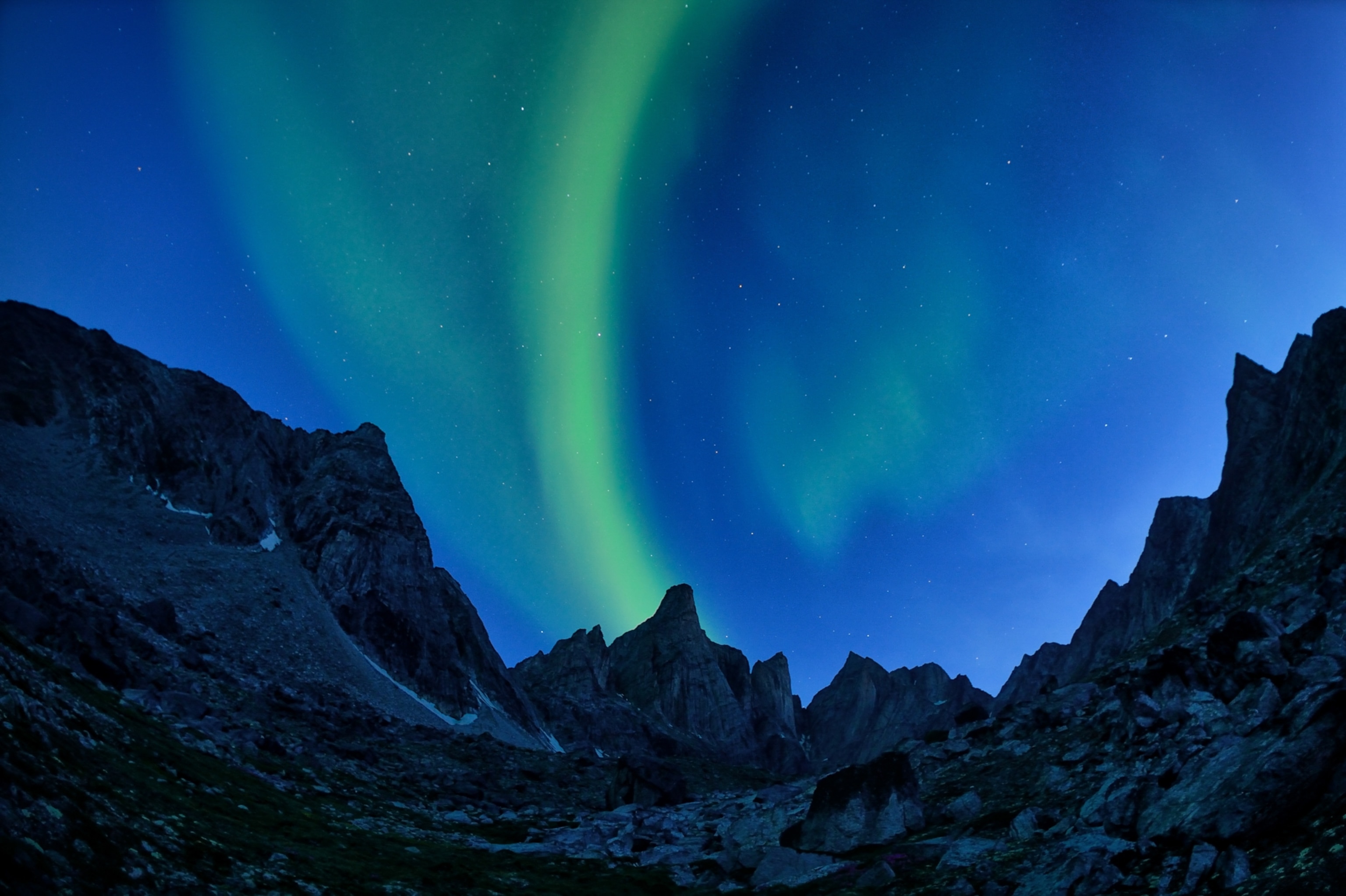 The aurora borealis bending towards the summit of a 2,000 foot-tall mountain peak.