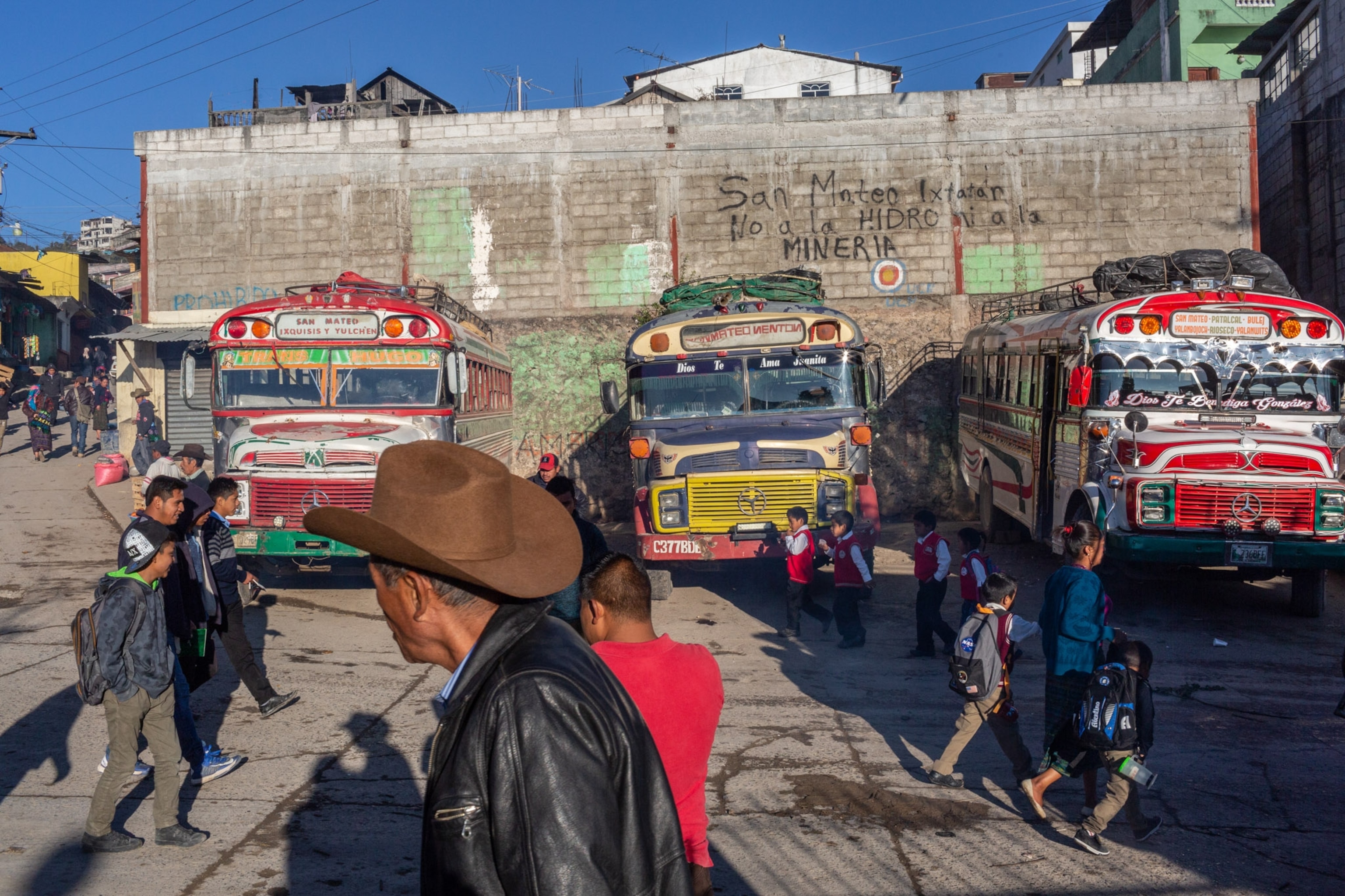 People walk by busses and graffiti on a wall.