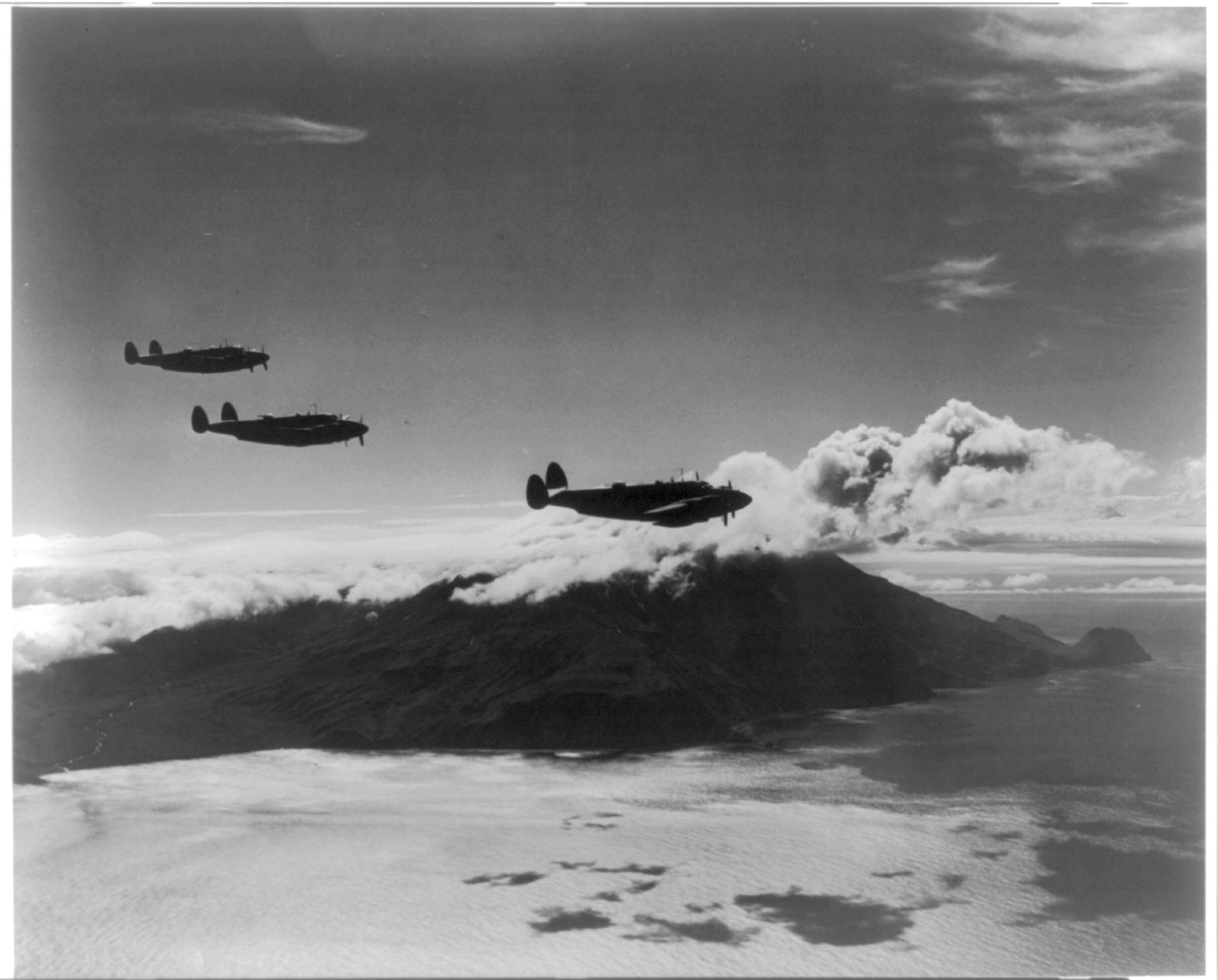 Three dual propeller bomber planes above mountains and sea.