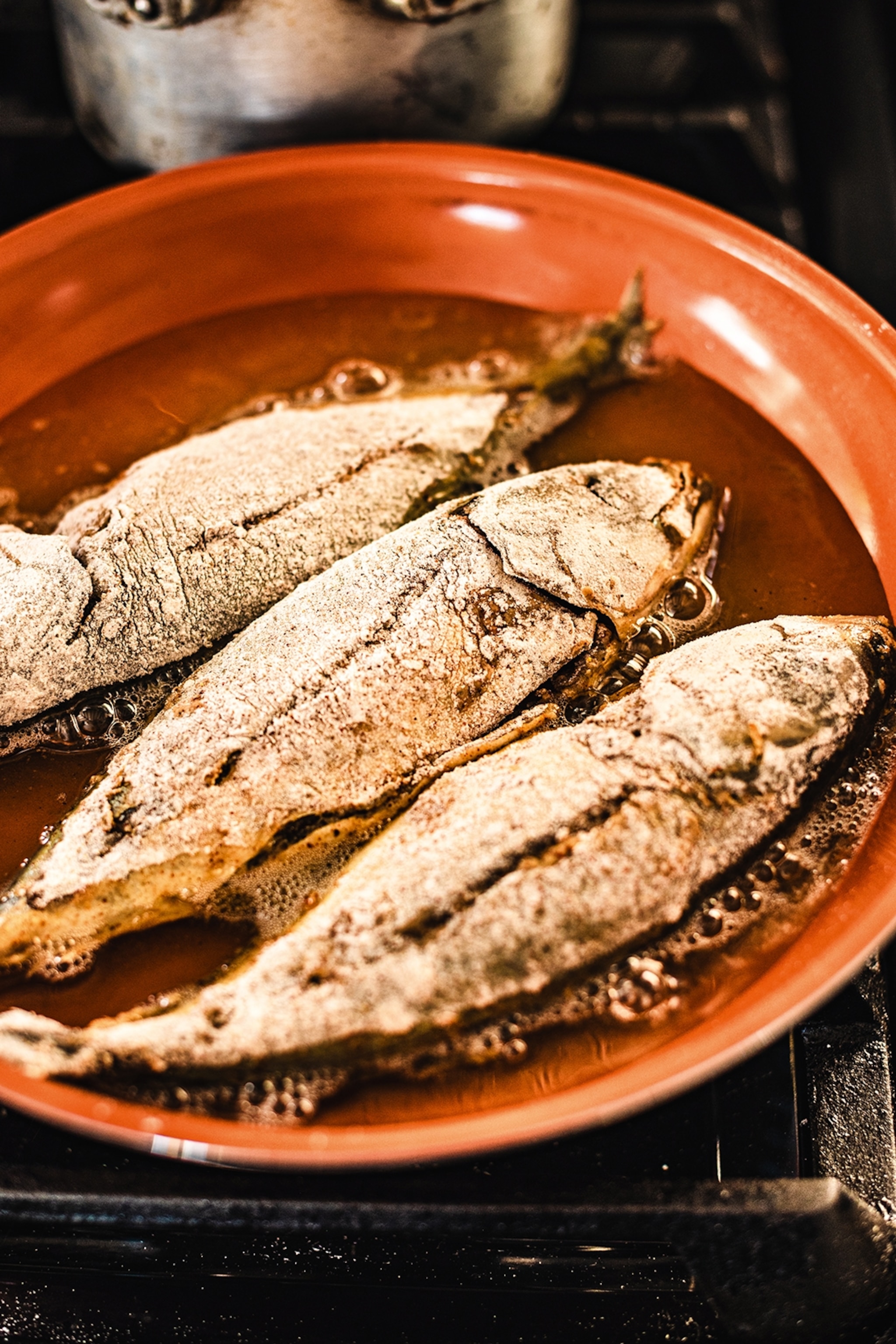 Three flour-dusted fish cooking in oil.