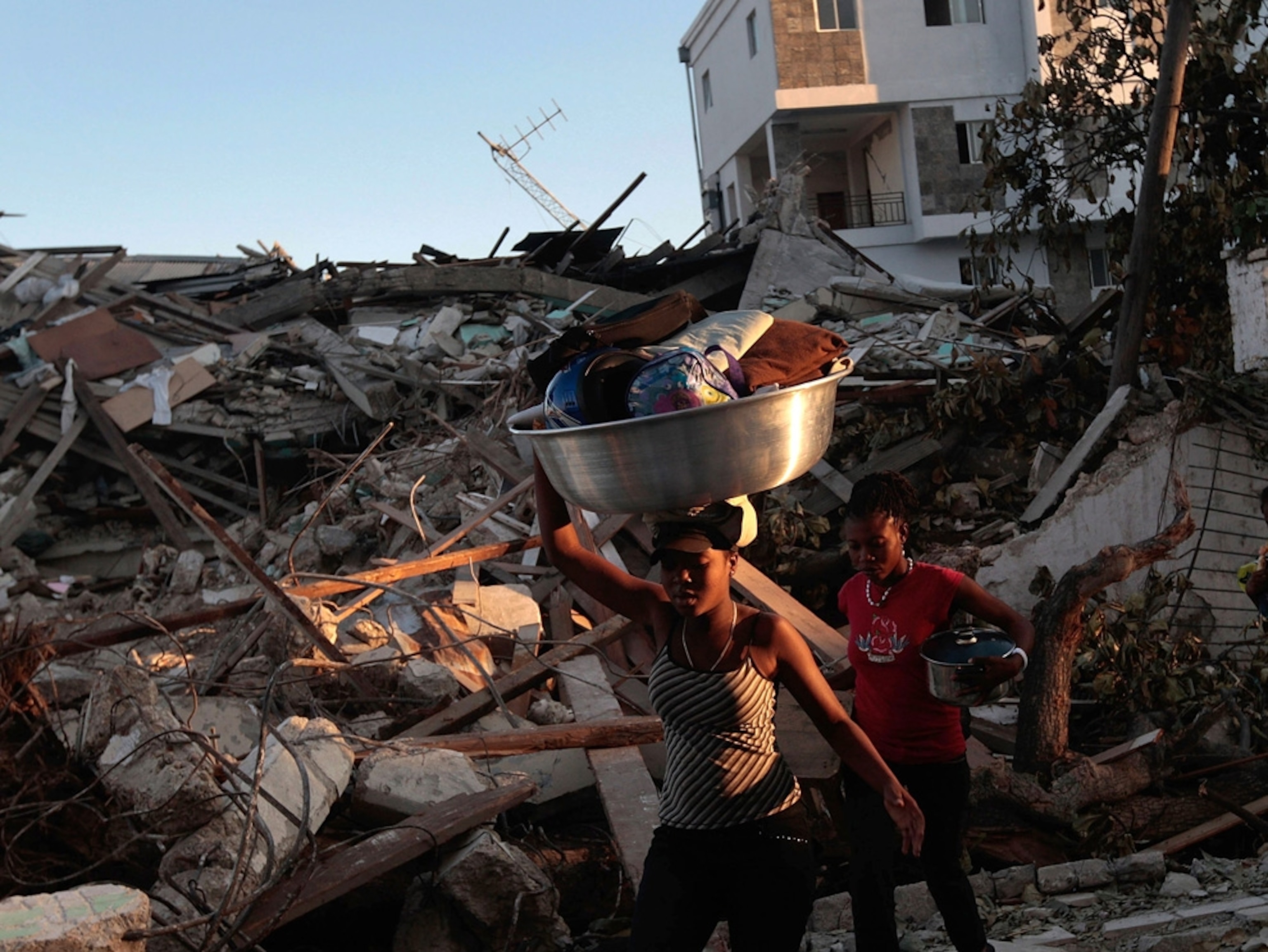 Women carry buckets of belongs through the rubble of a demolished neighborhood.