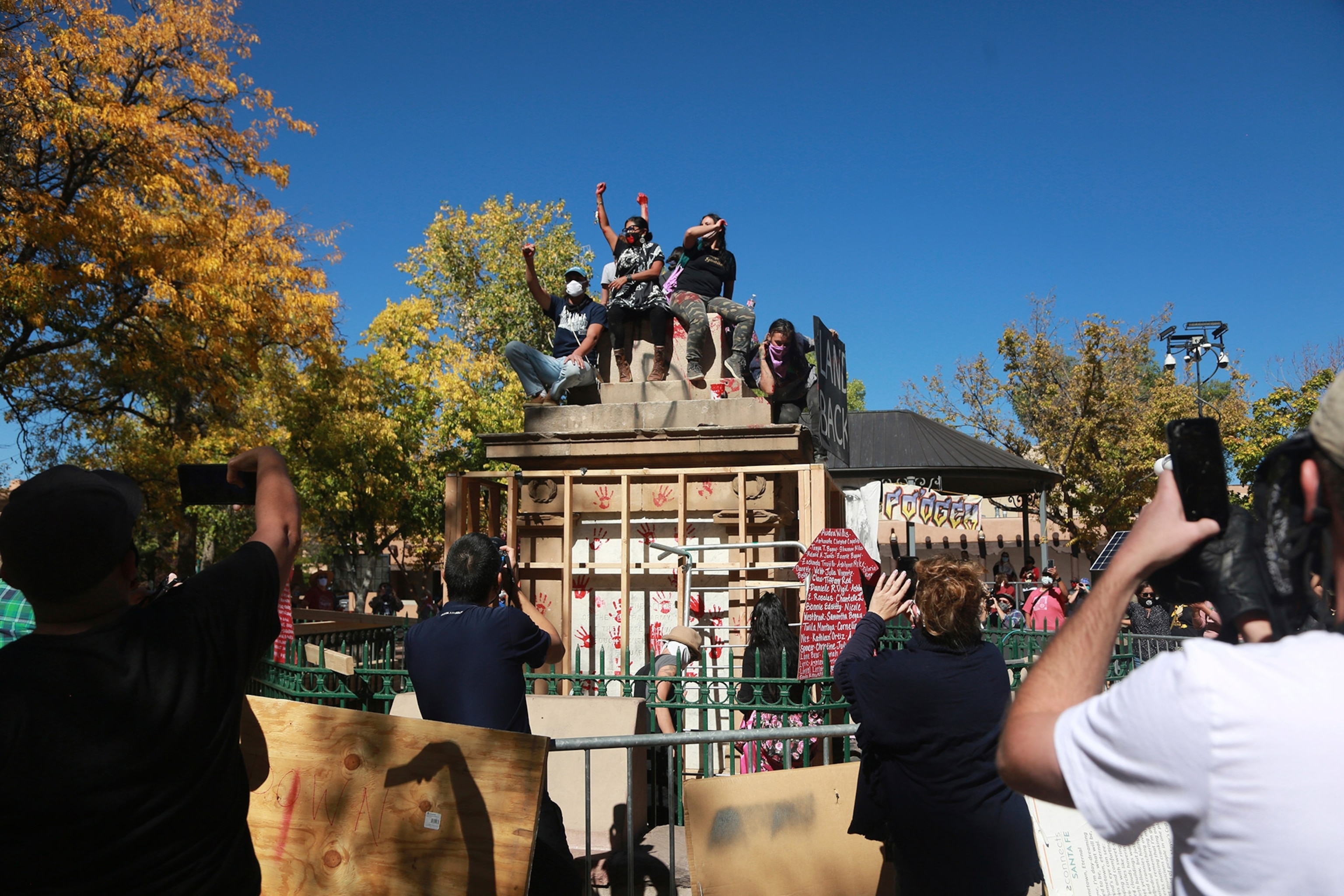 Demonstrators celebrate on the base of a stone obelisk torn down in Santa Fe, New Mexico