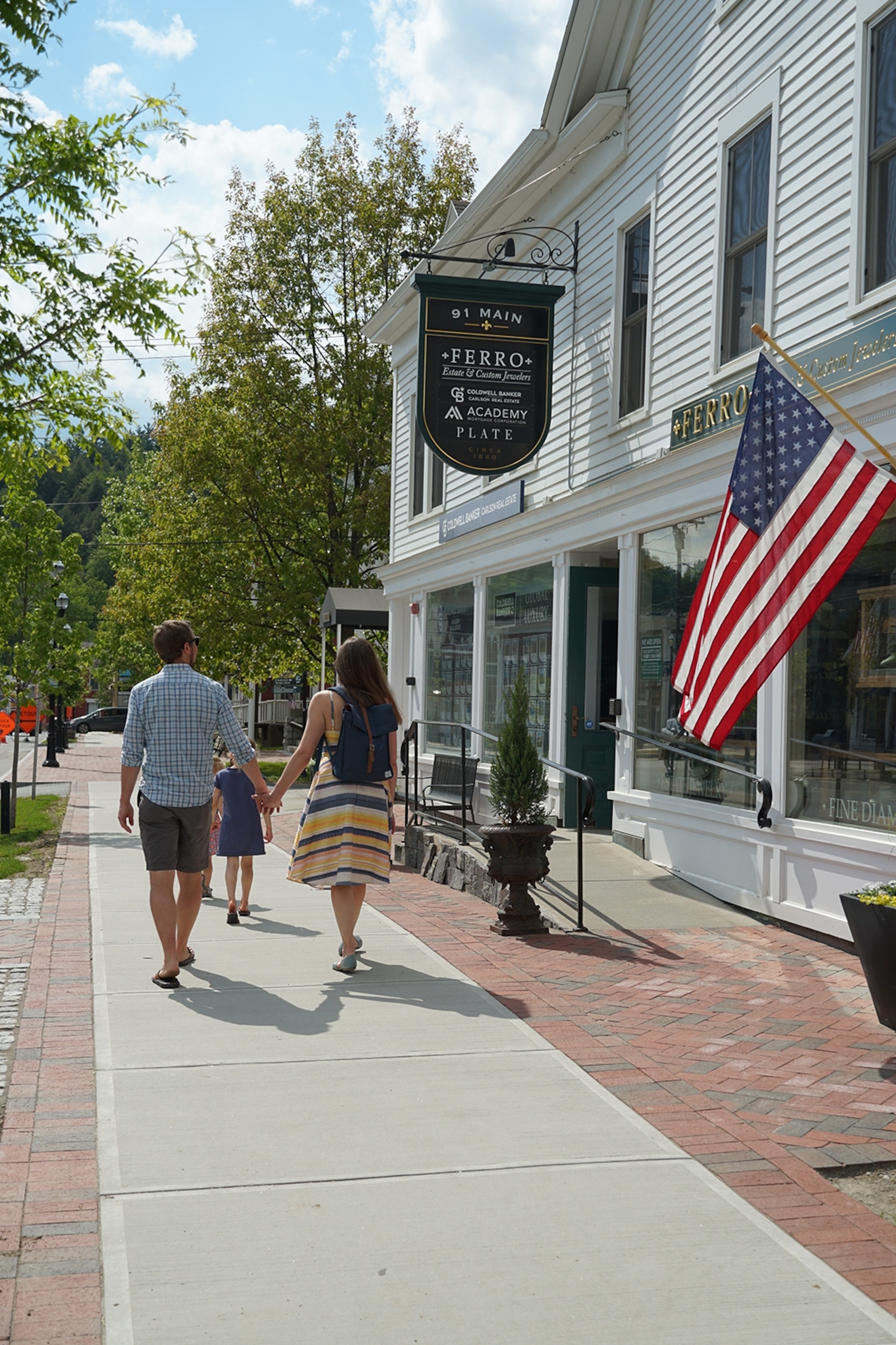 A couple walking in the downtown village of Stowe, Vermont, with a US flag.