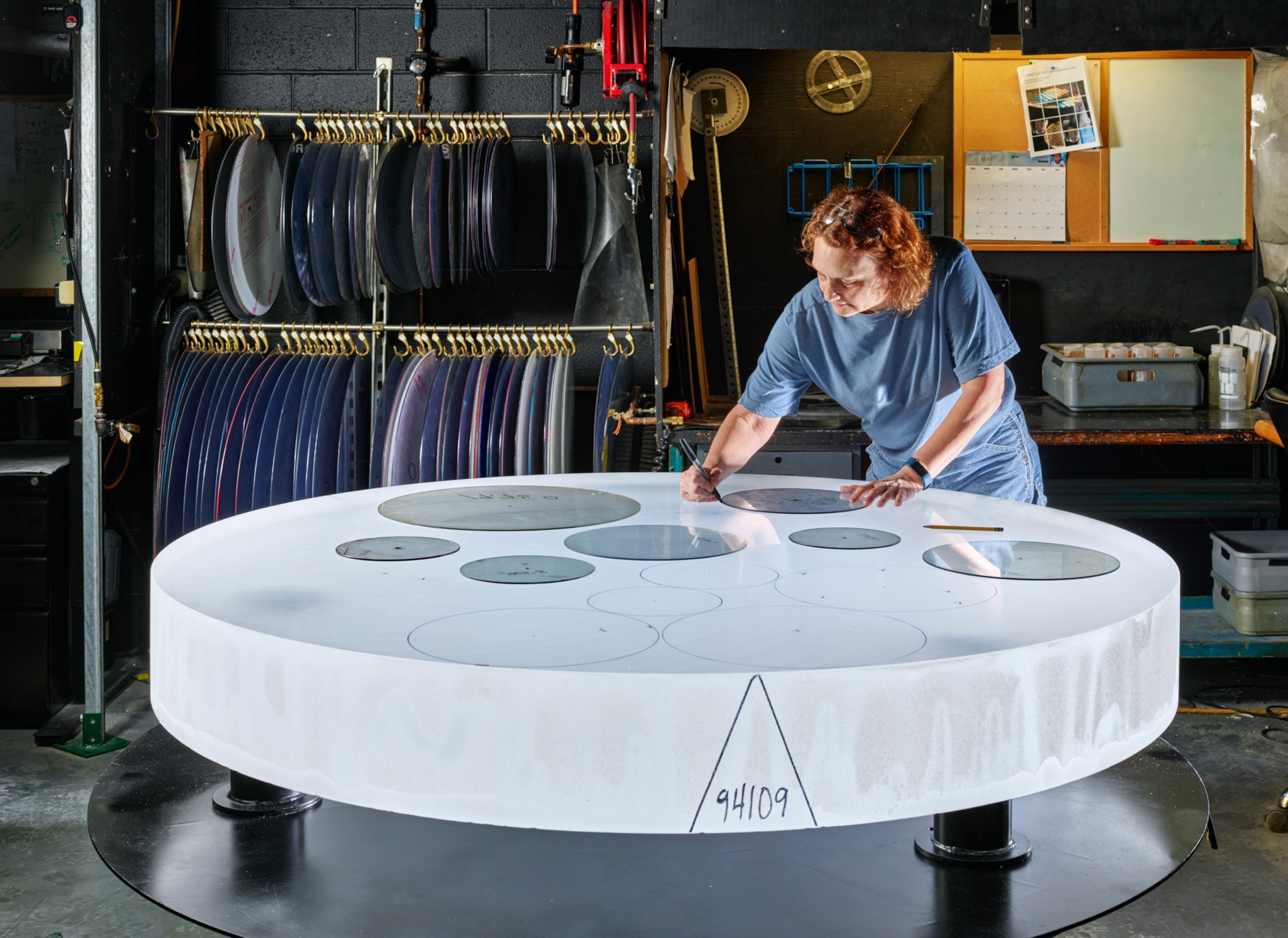 a woman stands over a large piece of glass drawing circles on the surface with templates.