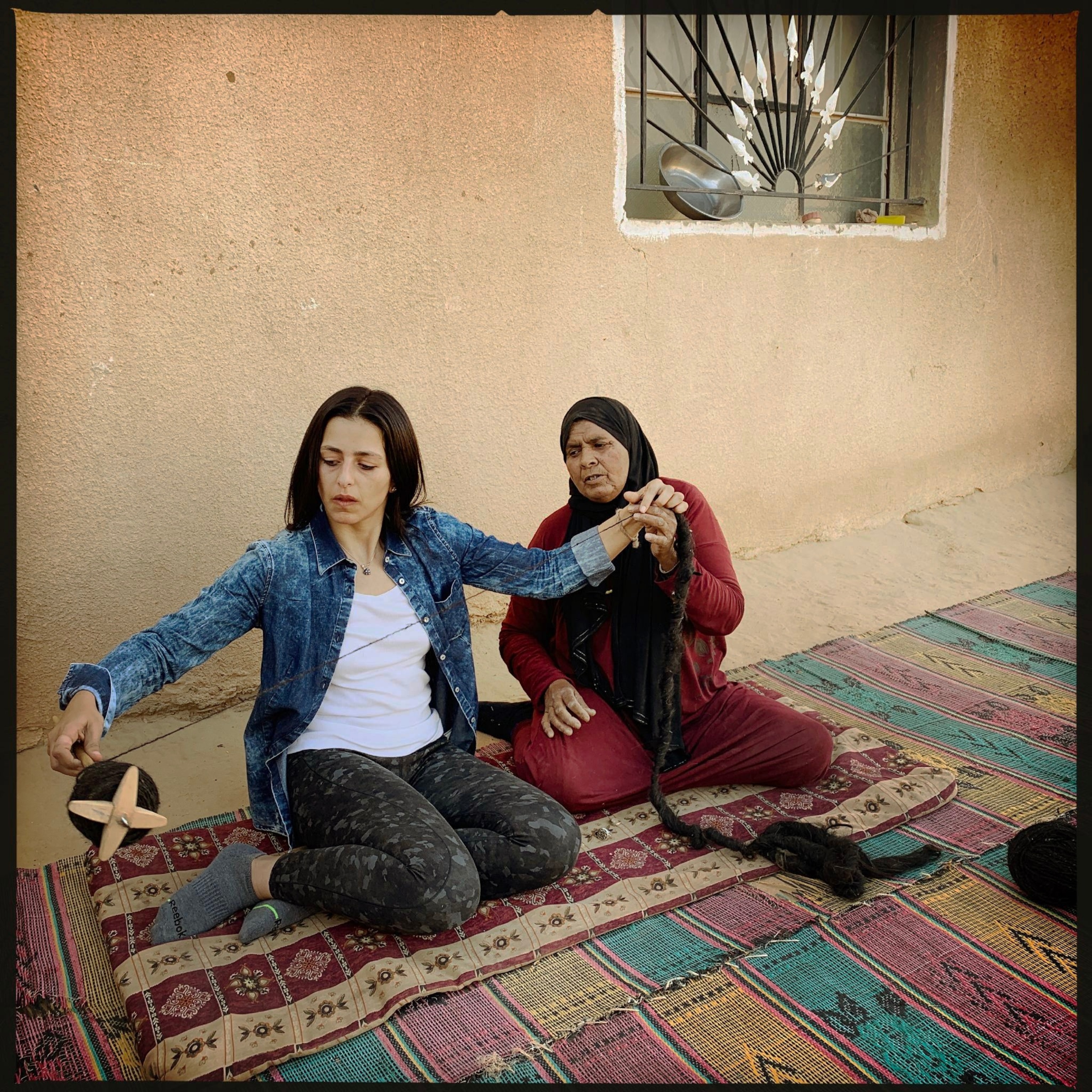 older woman with her dead covered and young without cover spinning wool