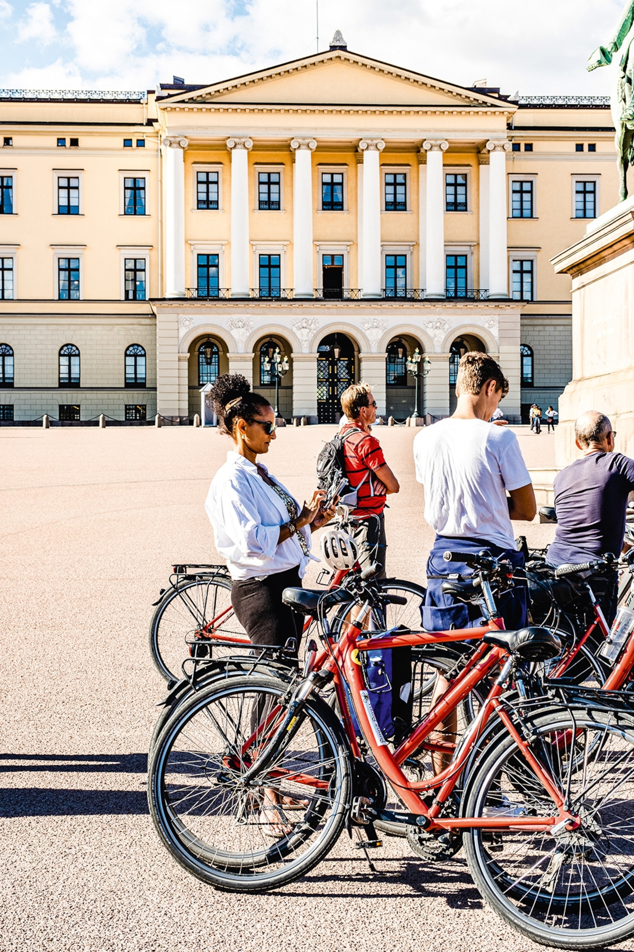 Tourists with bikes on the city cycling tour stop in front of The Royal Palace in Oslo.