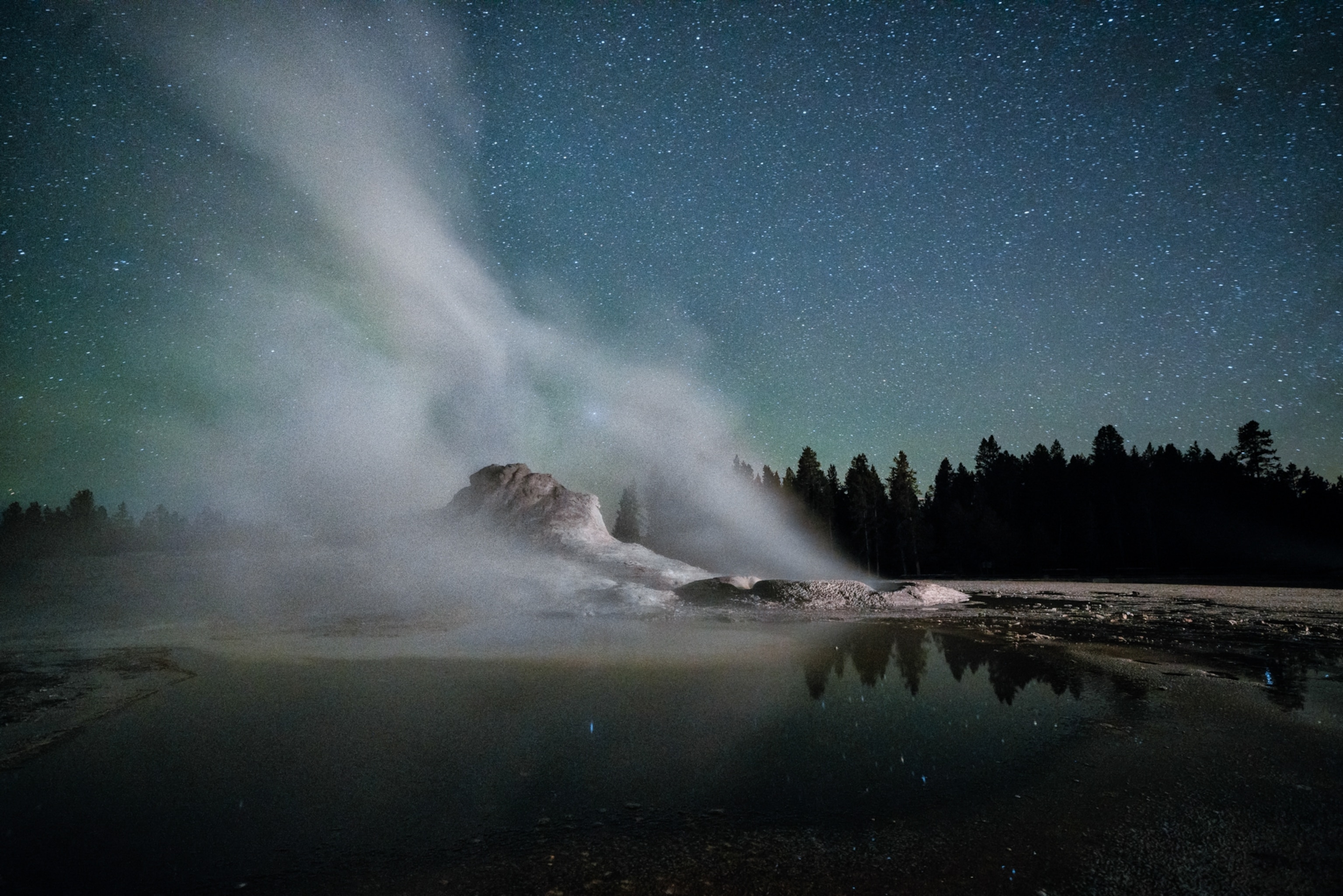Steam rising from a geyser towards a star filled sky.
